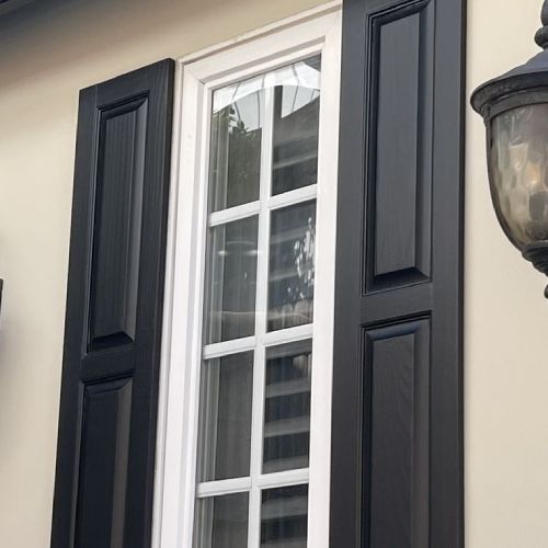 A window with black shutters and a lamp on the side of a house.