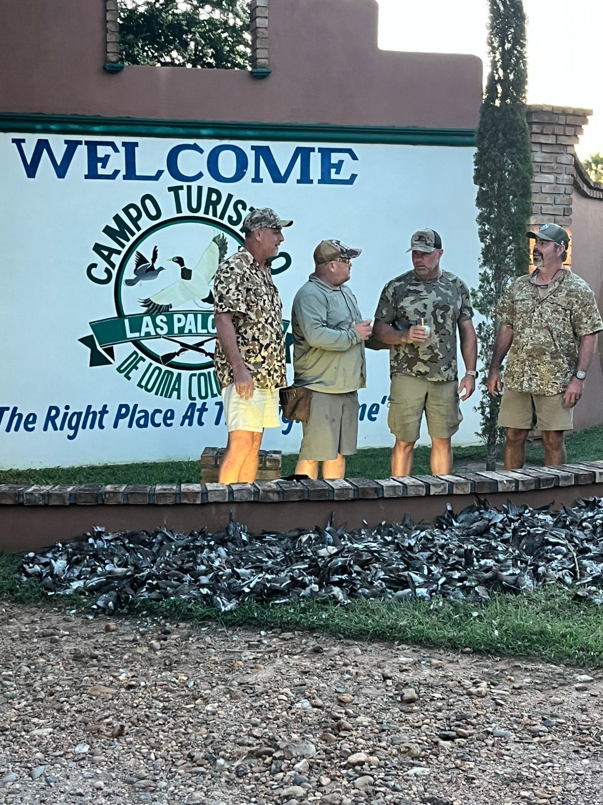 Four people standing on a stage in front of a Camp Tuffy welcome sign outdoors.