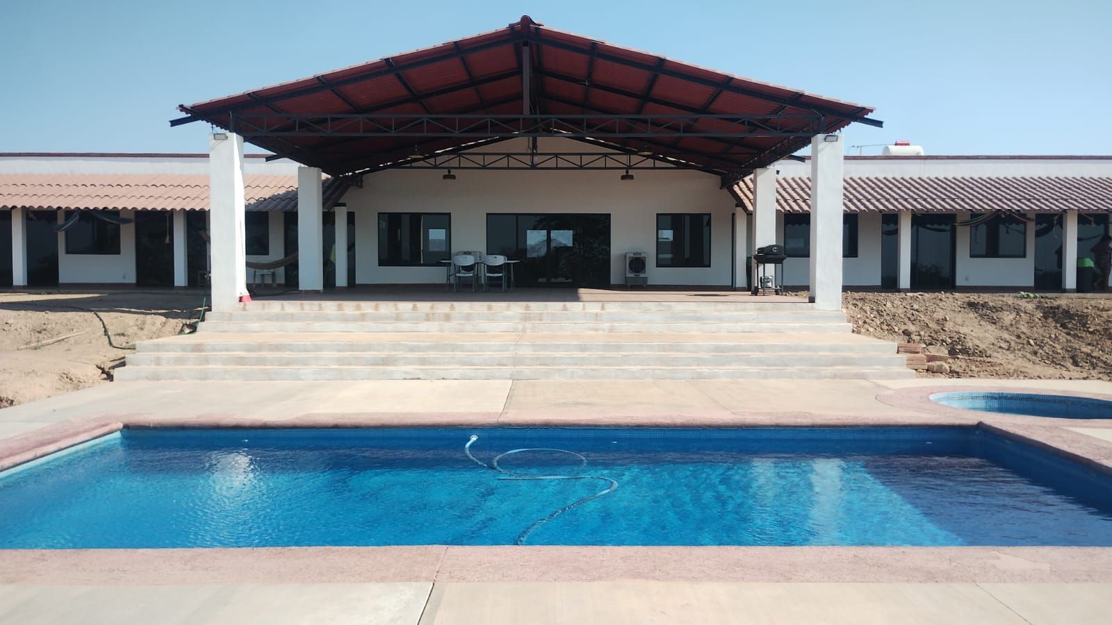 Swimming pool in front of a covered patio with a red roof and white columns