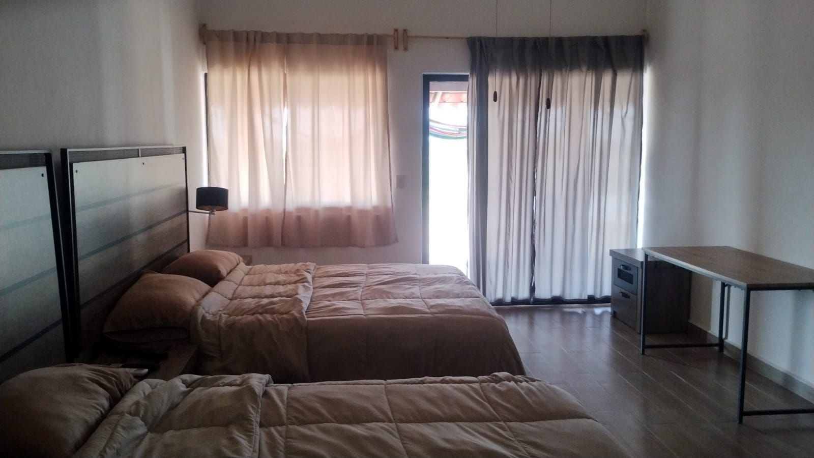 Hotel room with two twin beds, sheer curtains, sliding glass doors, and a desk by the window.