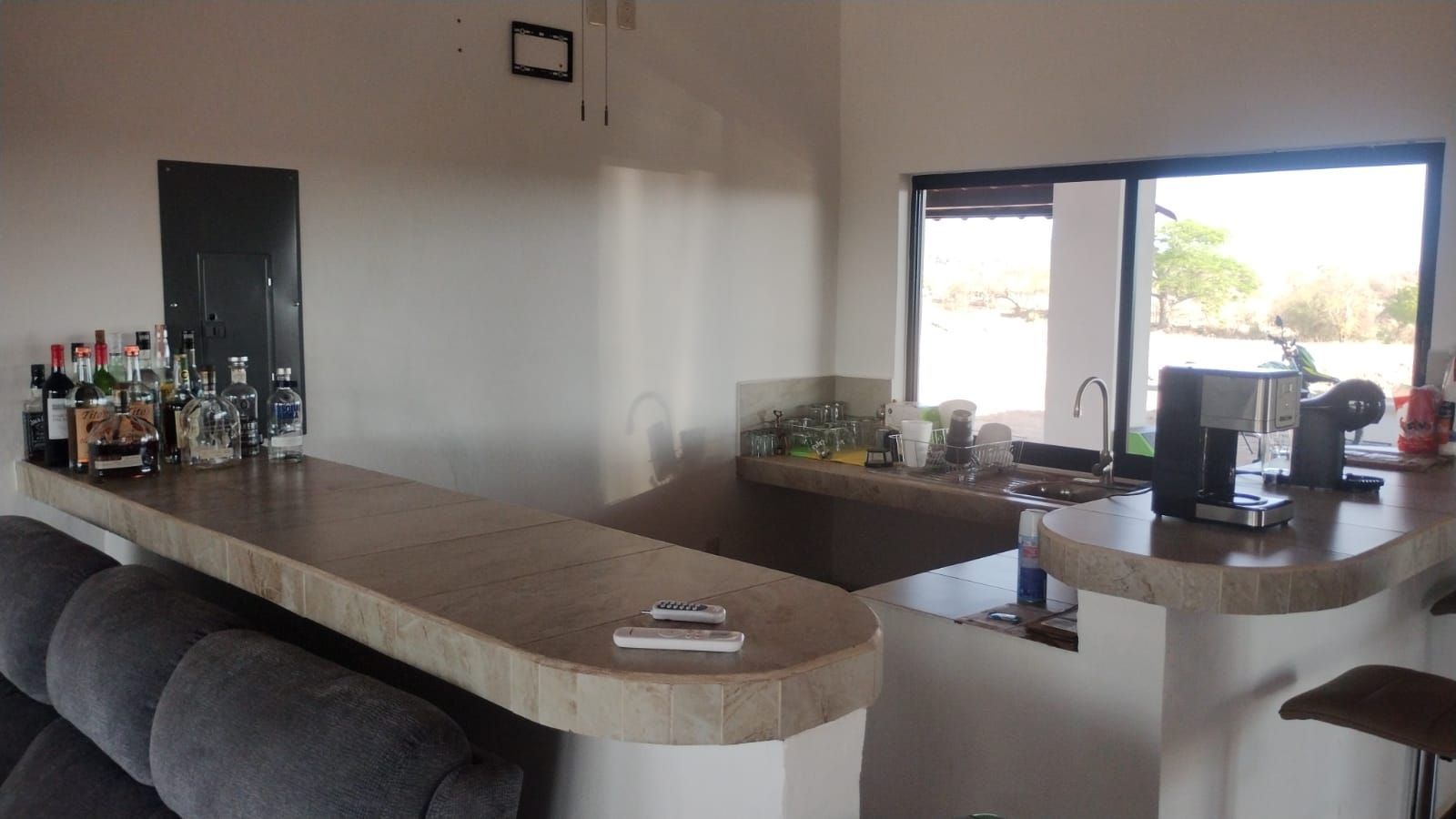 Modern kitchen with a long counter, bar stools, and a window overlooking an outdoor patio area