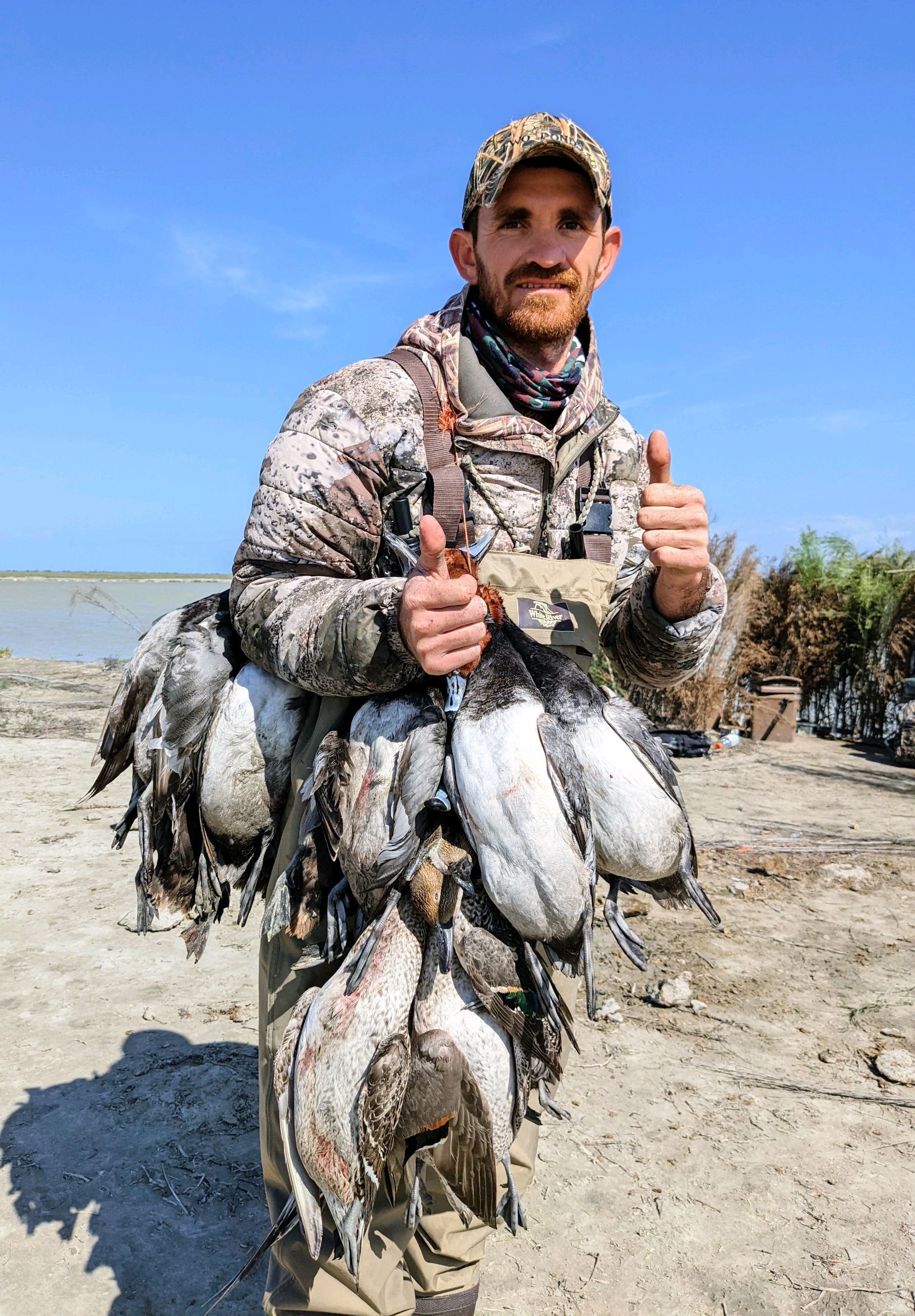 Man holding a large string of fish on a sandy beach under a clear blue sky