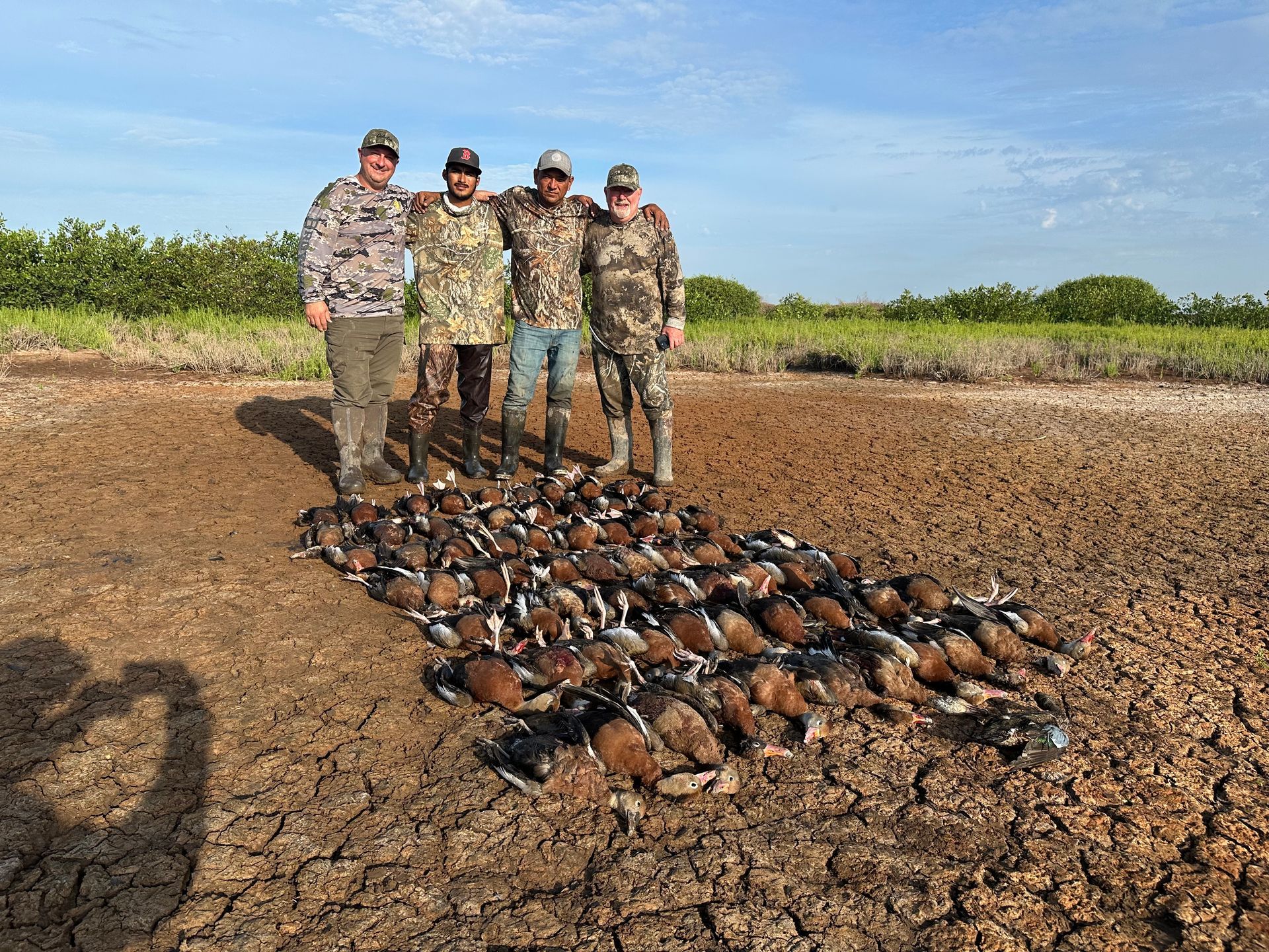 Four people standing on dry ground beside a large pile of harvested turtles under a clear sky