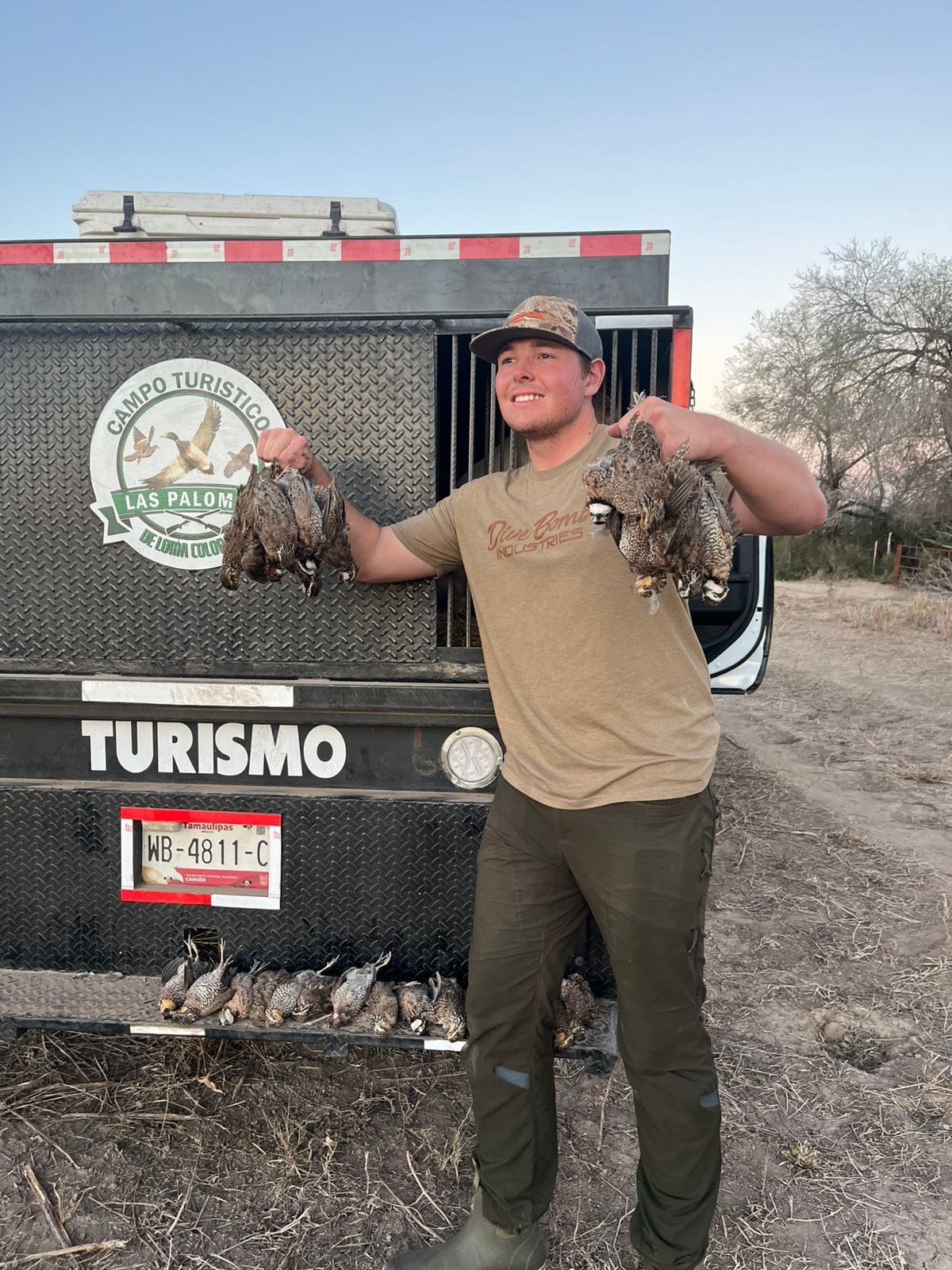 Man holding two birds in front of a hunting truck with a “Turismo” sign
