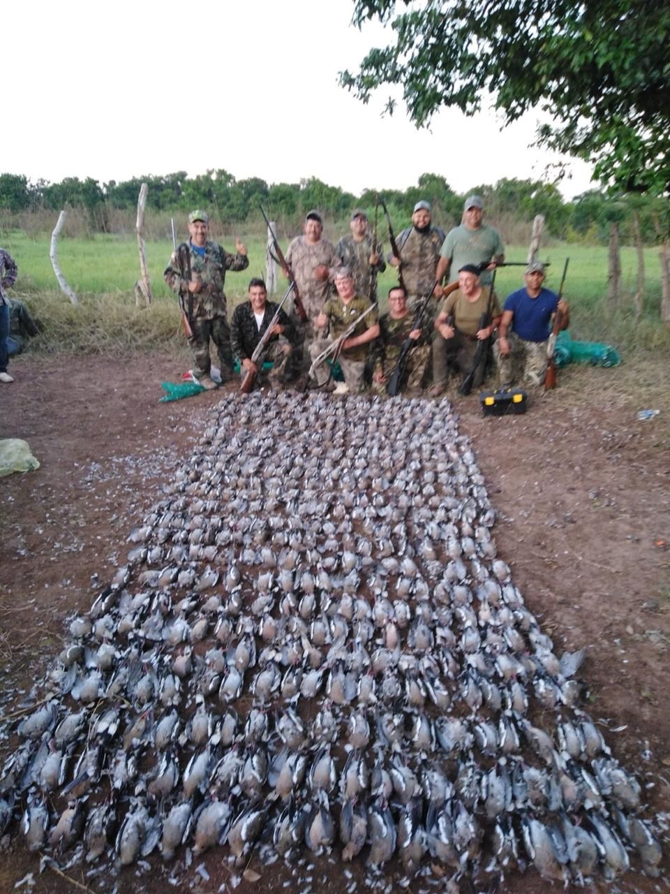 Group posing behind a large row of hunted birds laid out on the ground in a grassy field