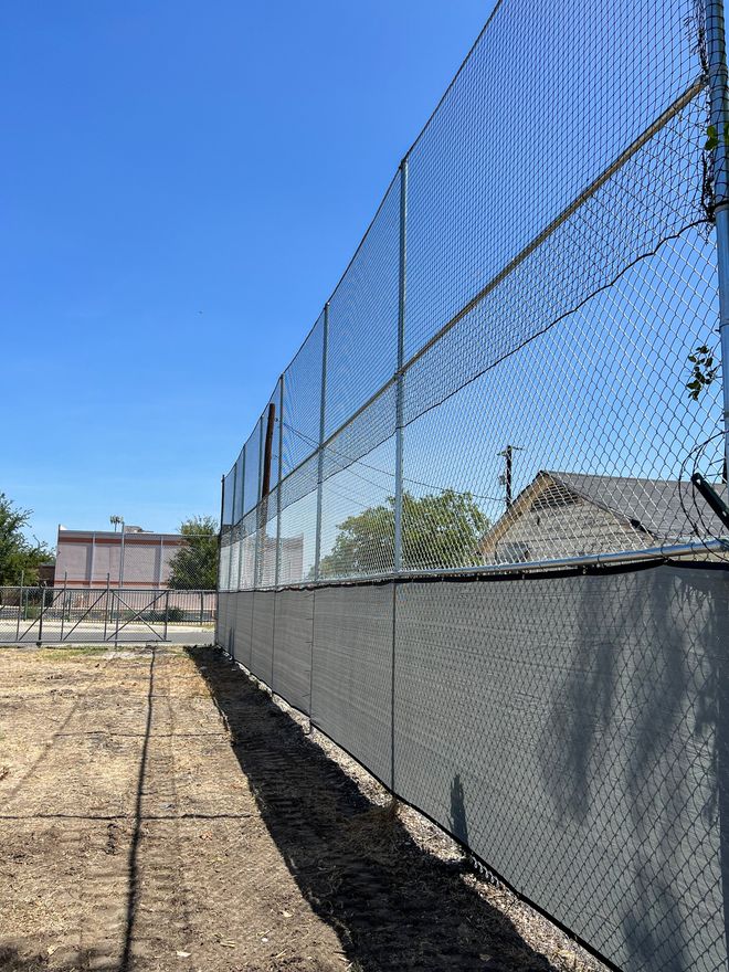 A chain link fence is surrounding a dirt field.