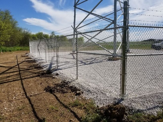 A chain link fence is surrounding a tower in a gravel area.