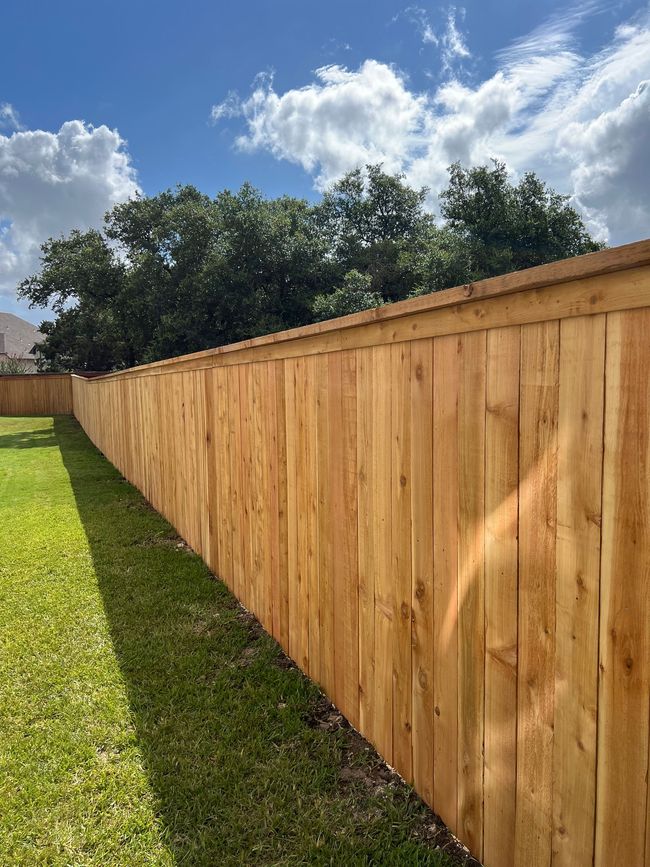 A long wooden fence surrounds a lush green yard.