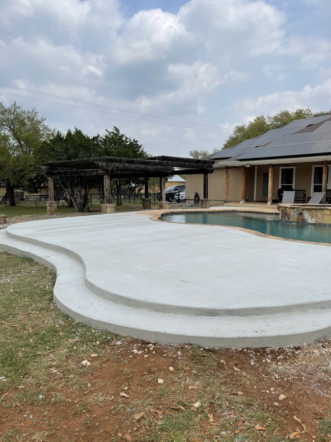 A concrete patio with steps leading to a swimming pool in front of a house.
