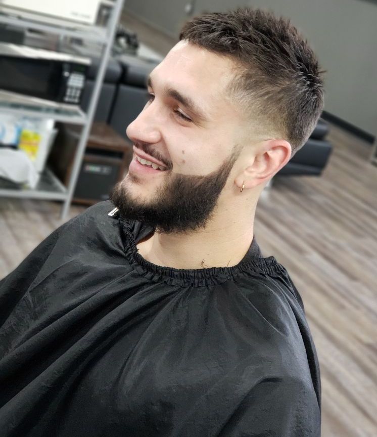 A man with a beard is getting his hair cut at a barber shop.