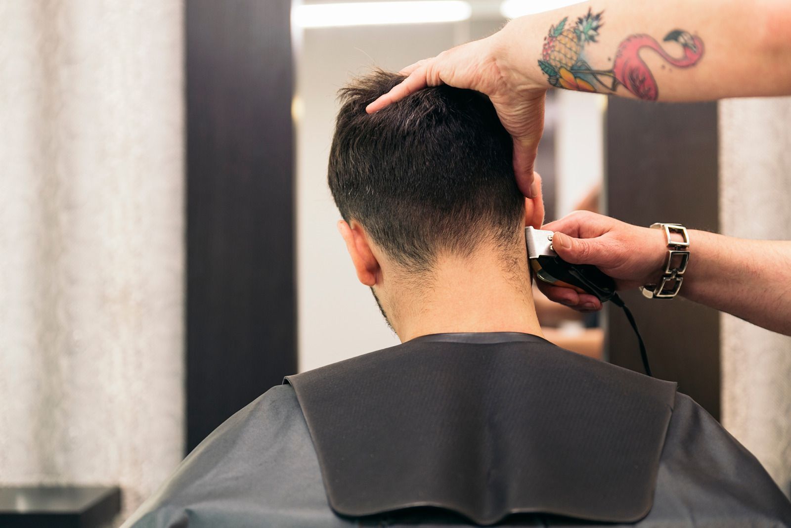 Barber giving a man a haircut with clippers; a tattoo of a flamingo is visible on the barber's arm.