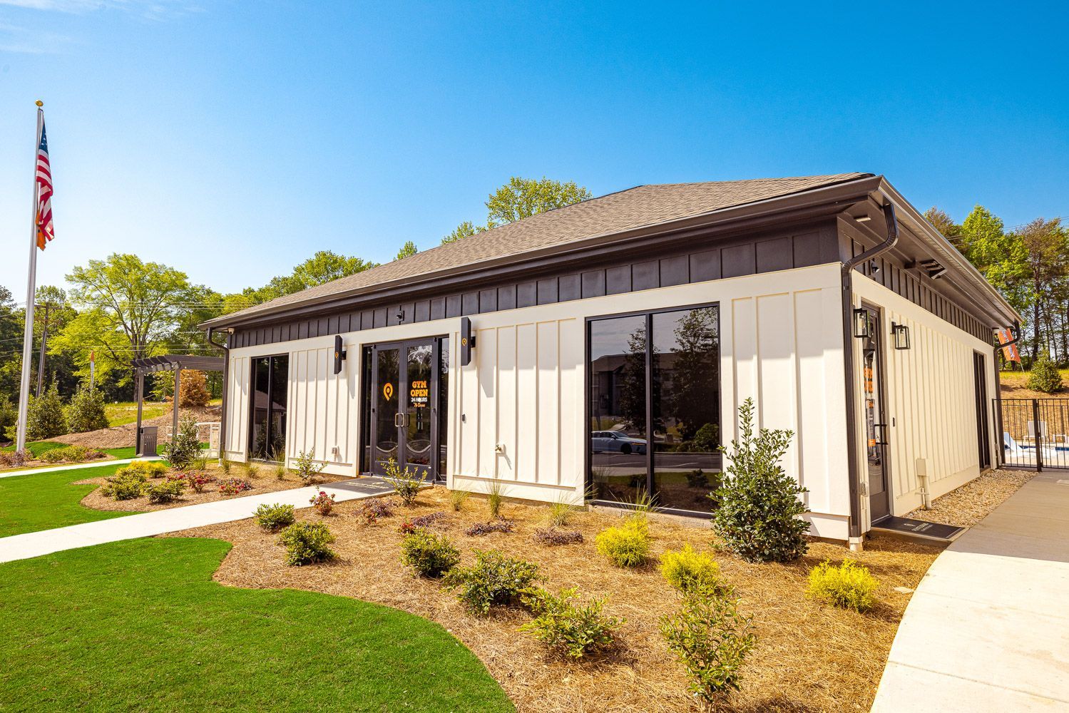 A small white building with a brown roof and a flag in front of it at Pointe Grand at Heath Brook.