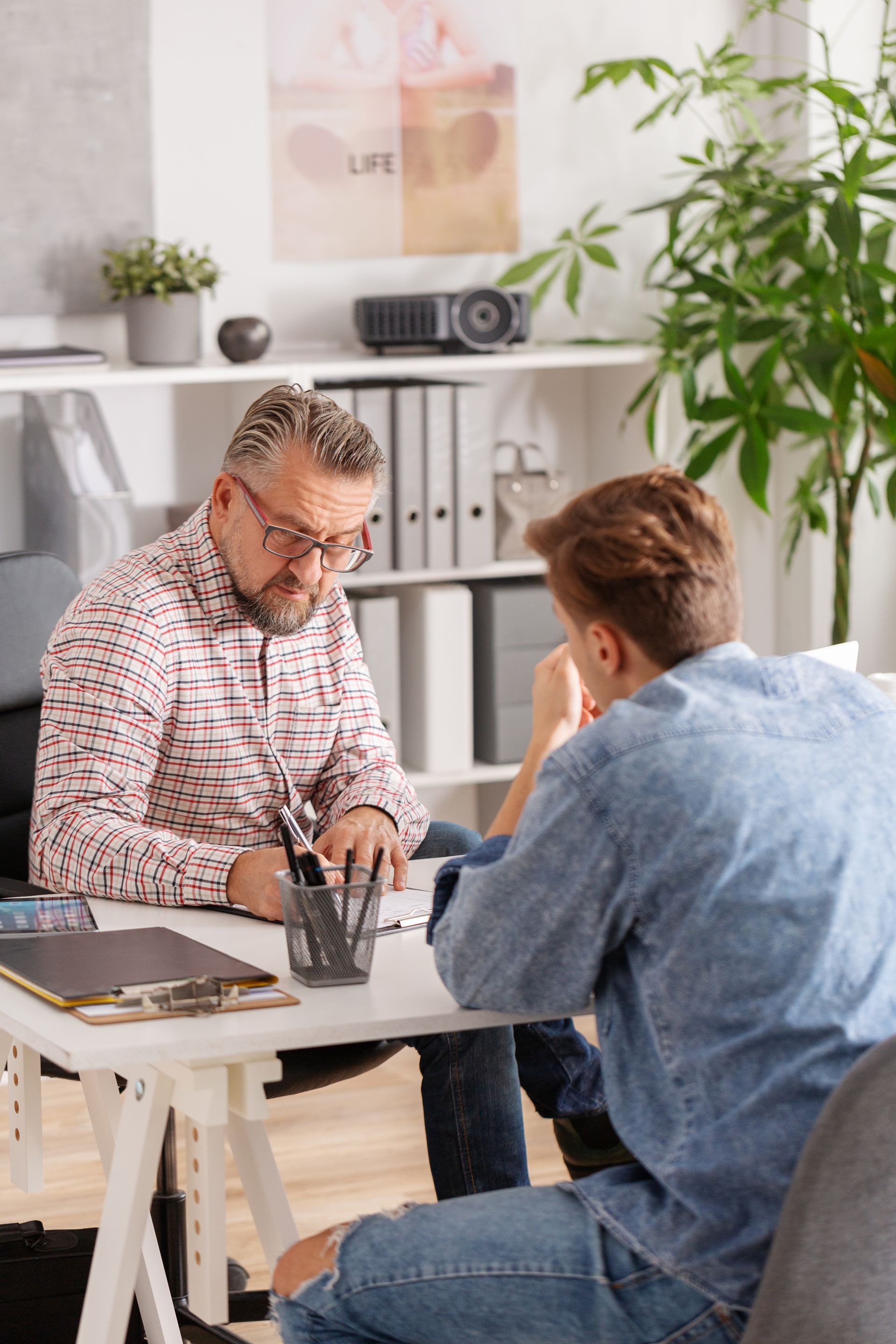 Two men are sitting at a table talking to each other.