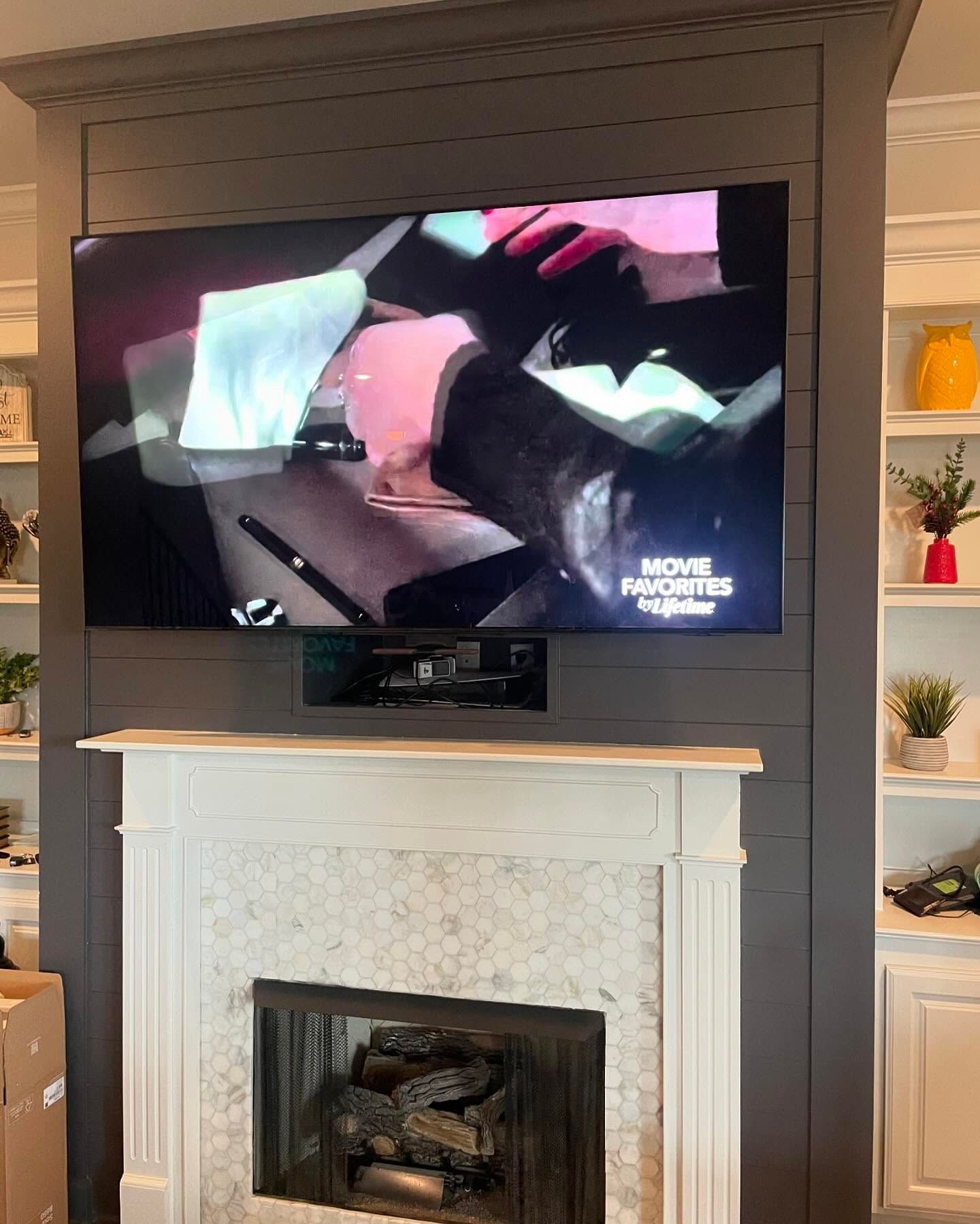 TV mounted above a fireplace, dark paneling, built-in shelves on each side with decorations.