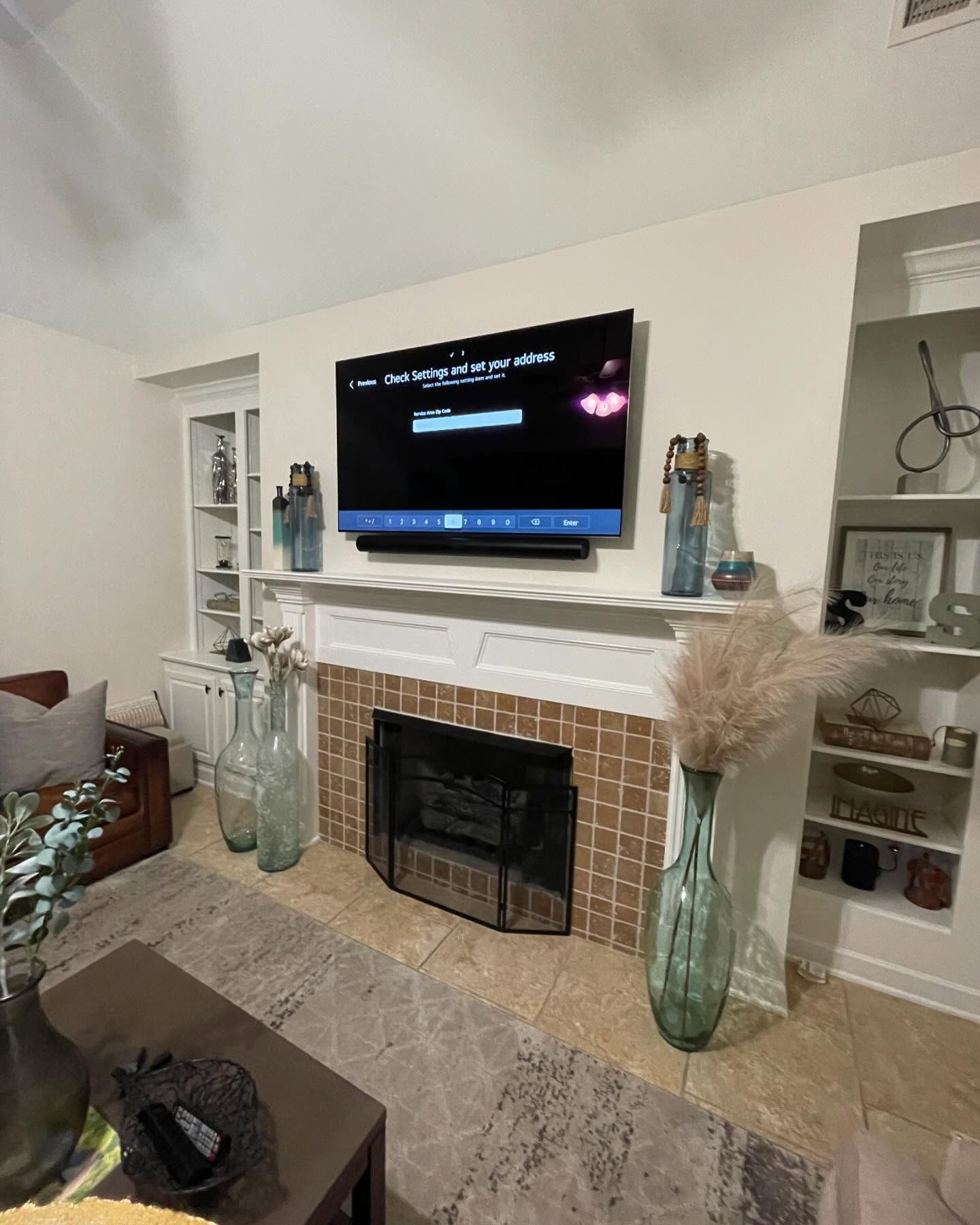 Living room with TV above fireplace, vases with pampas grass and decor.