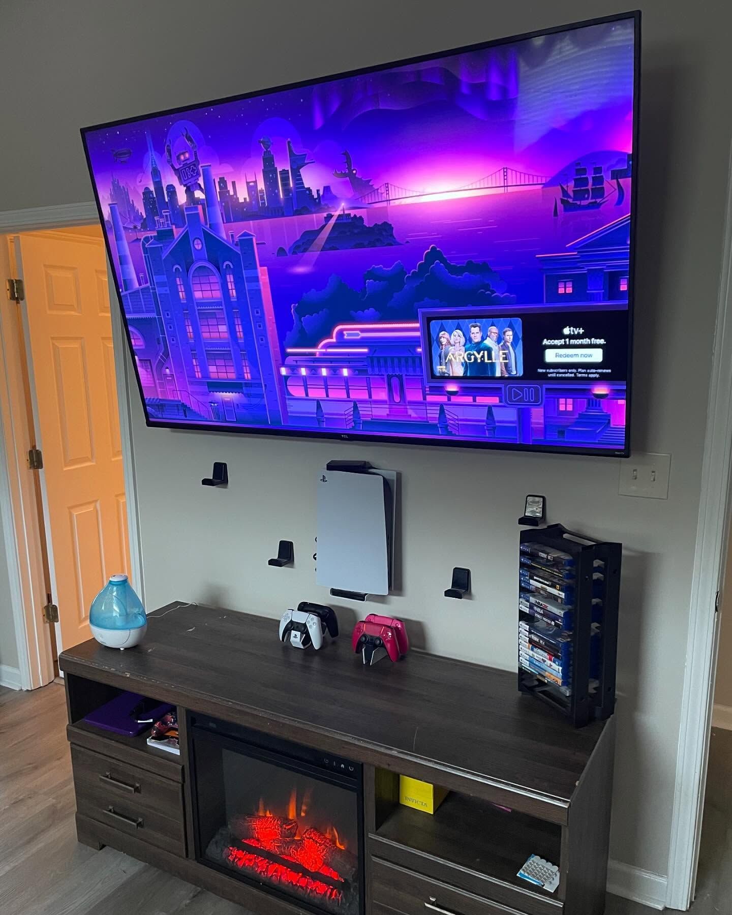 TV setup: large screen, purple/blue graphic, above console. PS5, controllers, and fireplace on a brown cabinet.