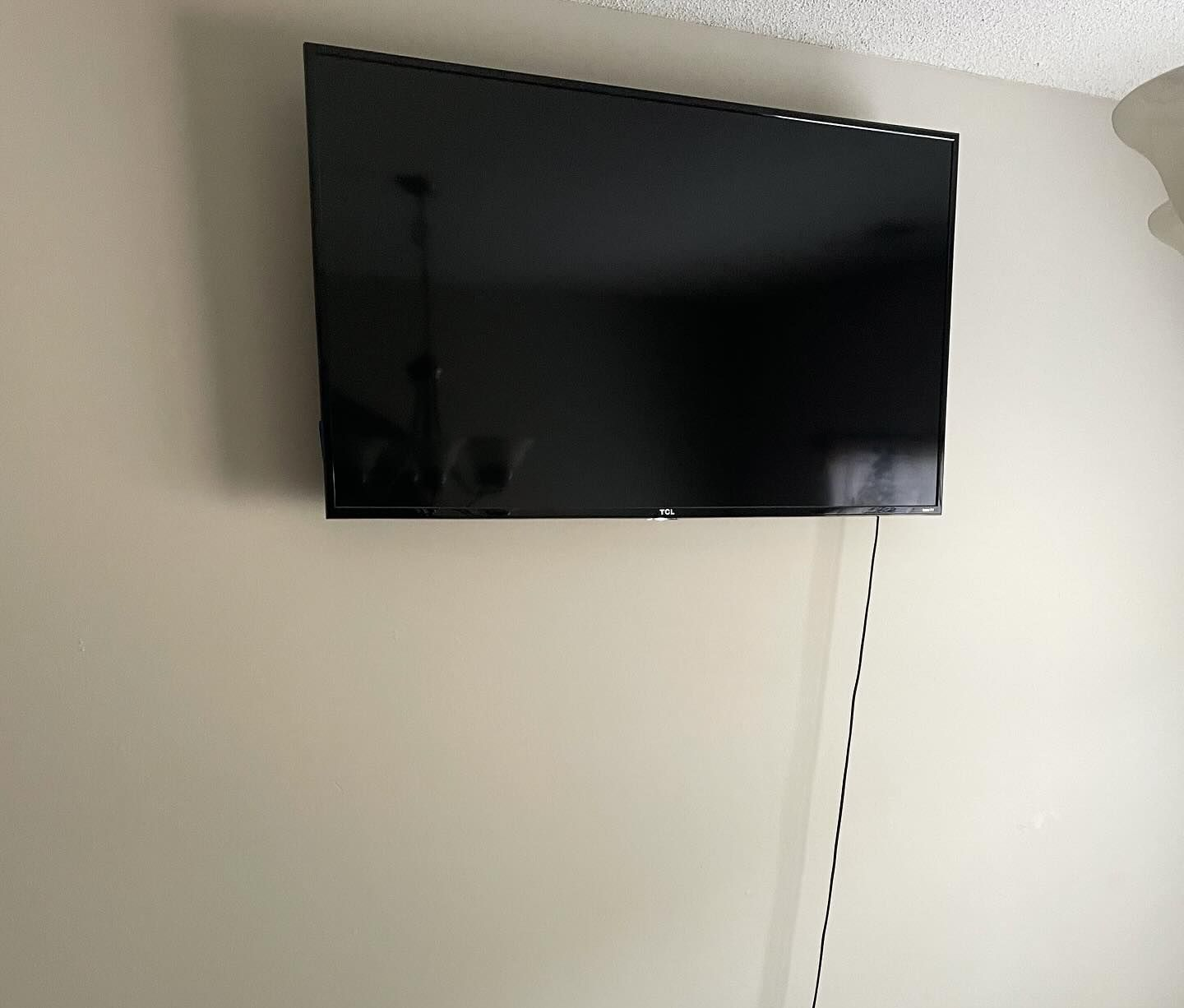 A flat-screen TV mounted on a beige wall, with a visible power cord hanging down.