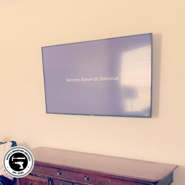TV mounted above a wooden dresser, displaying a welcome message on a light beige wall.