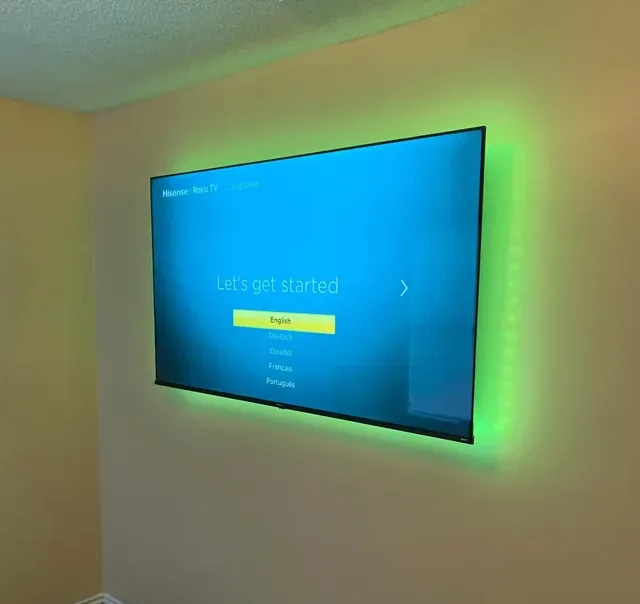 A large TV is mounted above a fireplace on a beige wall in a living room.