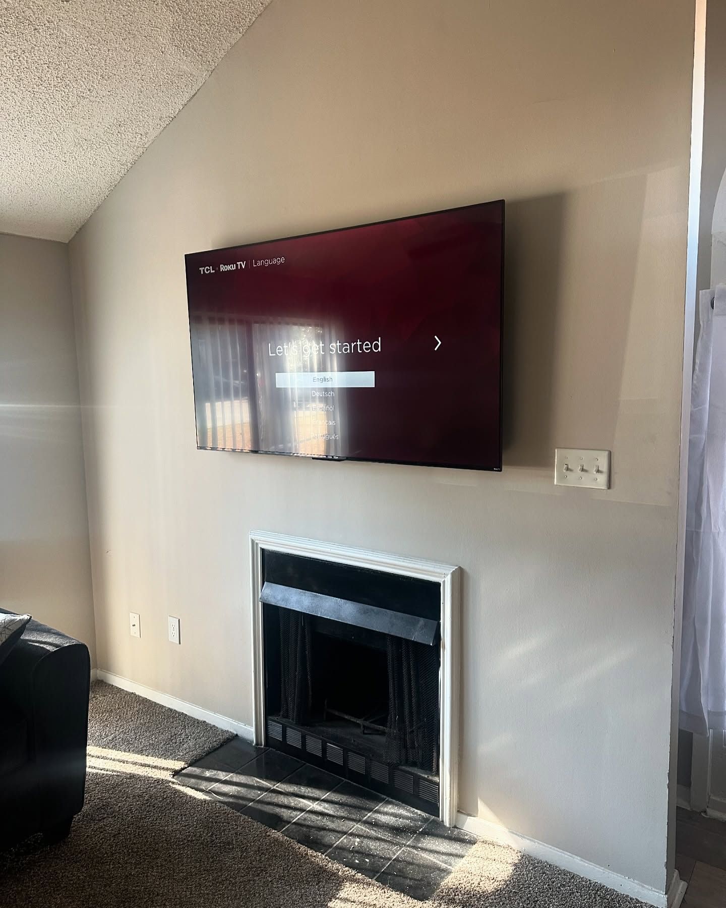 A large TV is mounted above a fireplace on a beige wall in a living room.