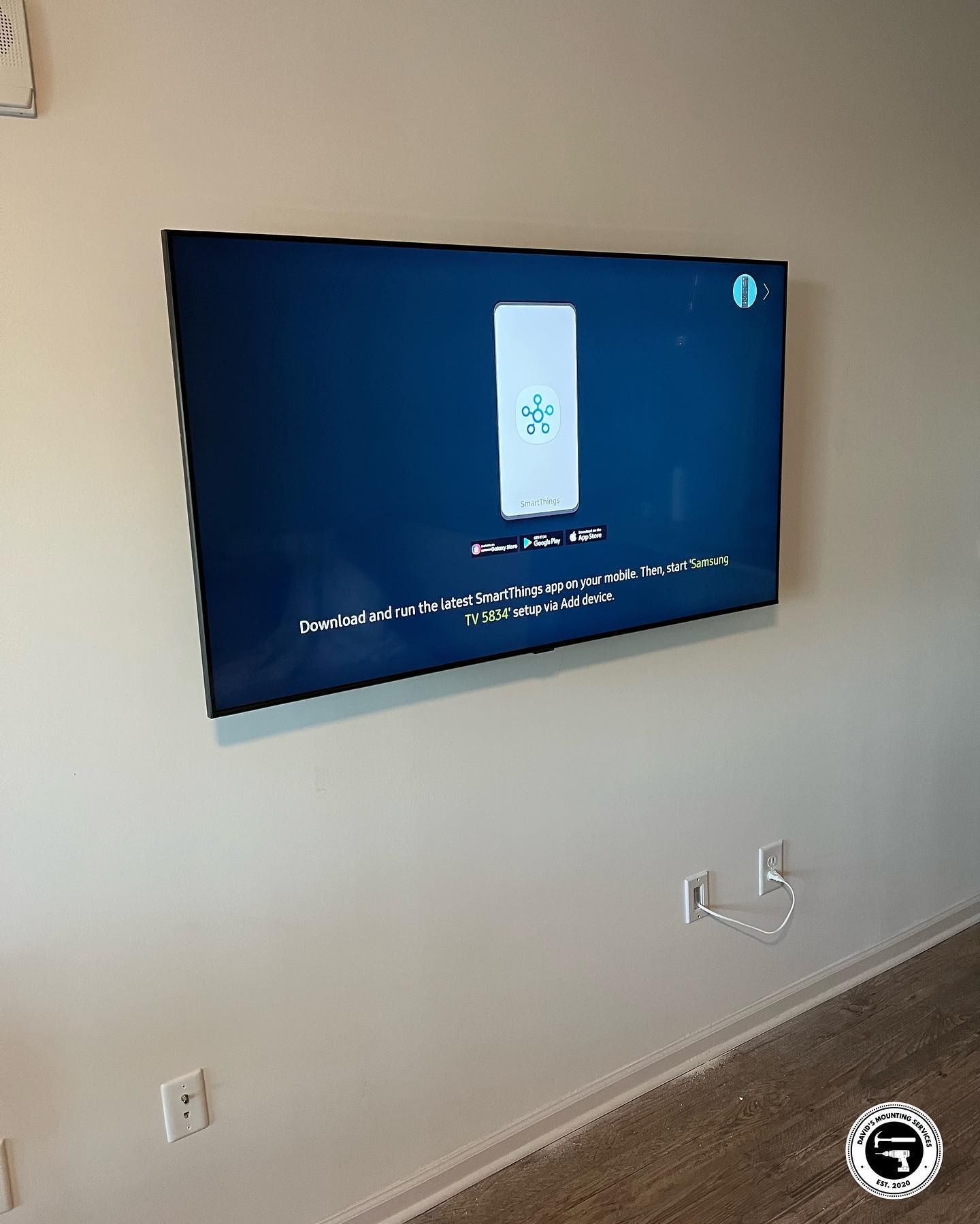 Wall-mounted TV with a blue screen displaying setup instructions; a white wall with electrical outlets visible.