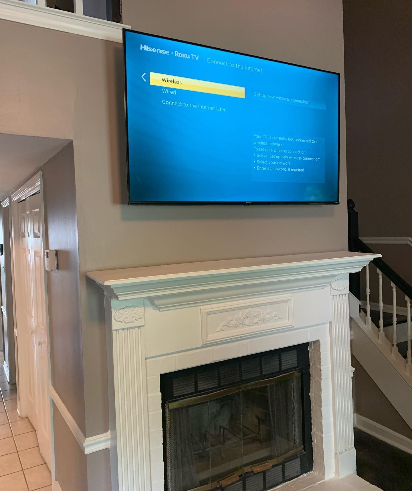 A flat-screen TV mounted above a white fireplace, displaying a blue screen. Interior setting.