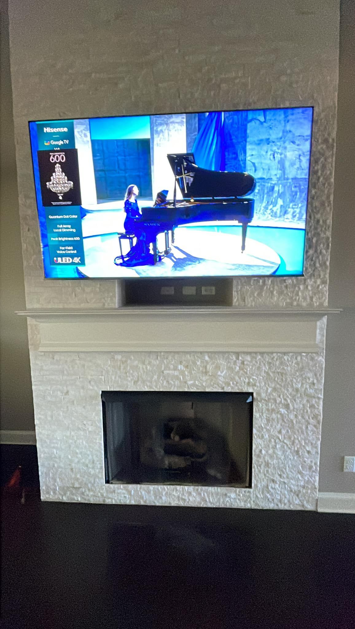 TV above a fireplace showing a pianist. The fireplace has a shiny white surface.