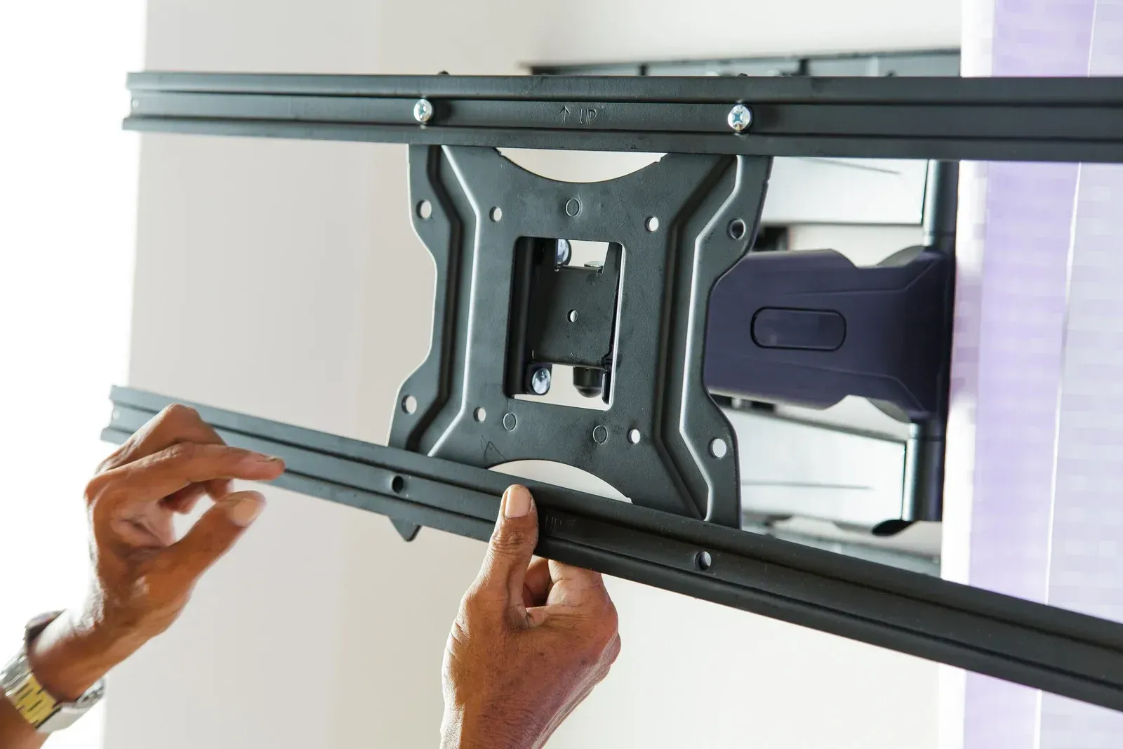 Hands installing a black TV mount on a wall.