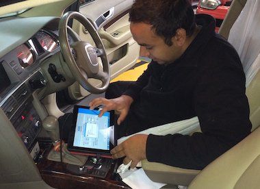 A man is sitting in the driver 's seat of a car using a tablet.