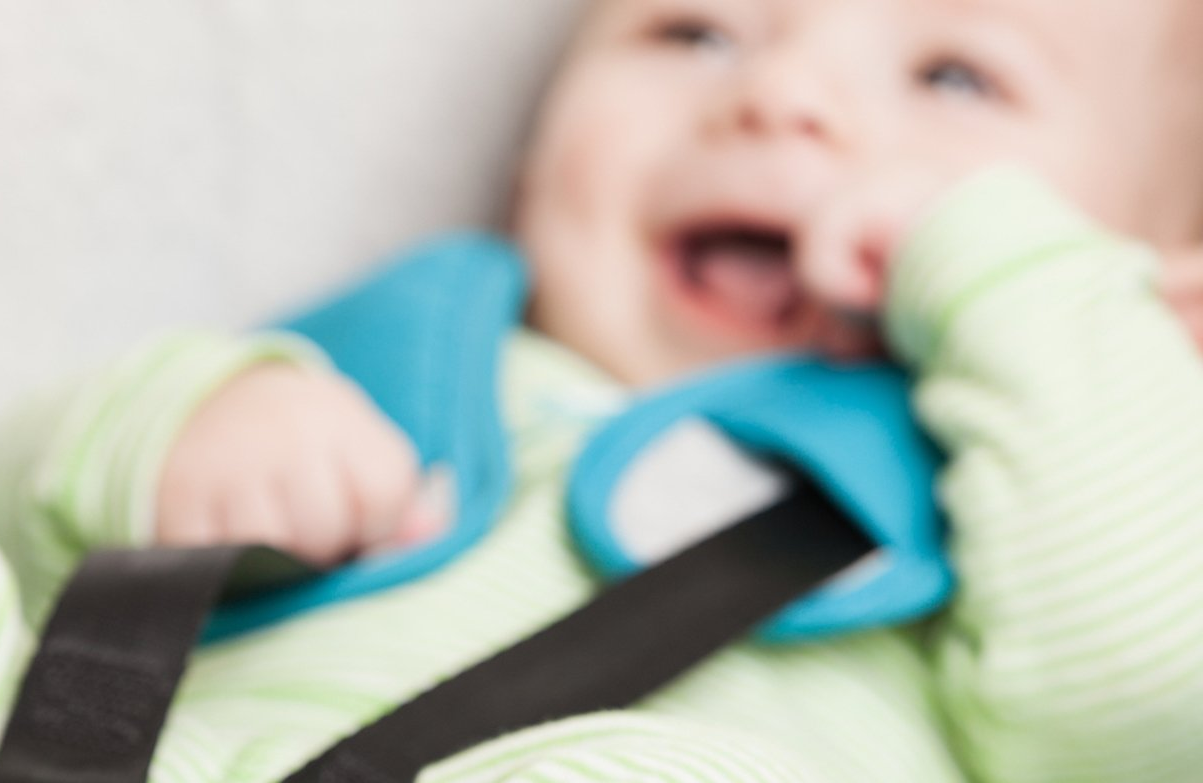 A baby is sitting in a car seat with a blue toy in his mouth.