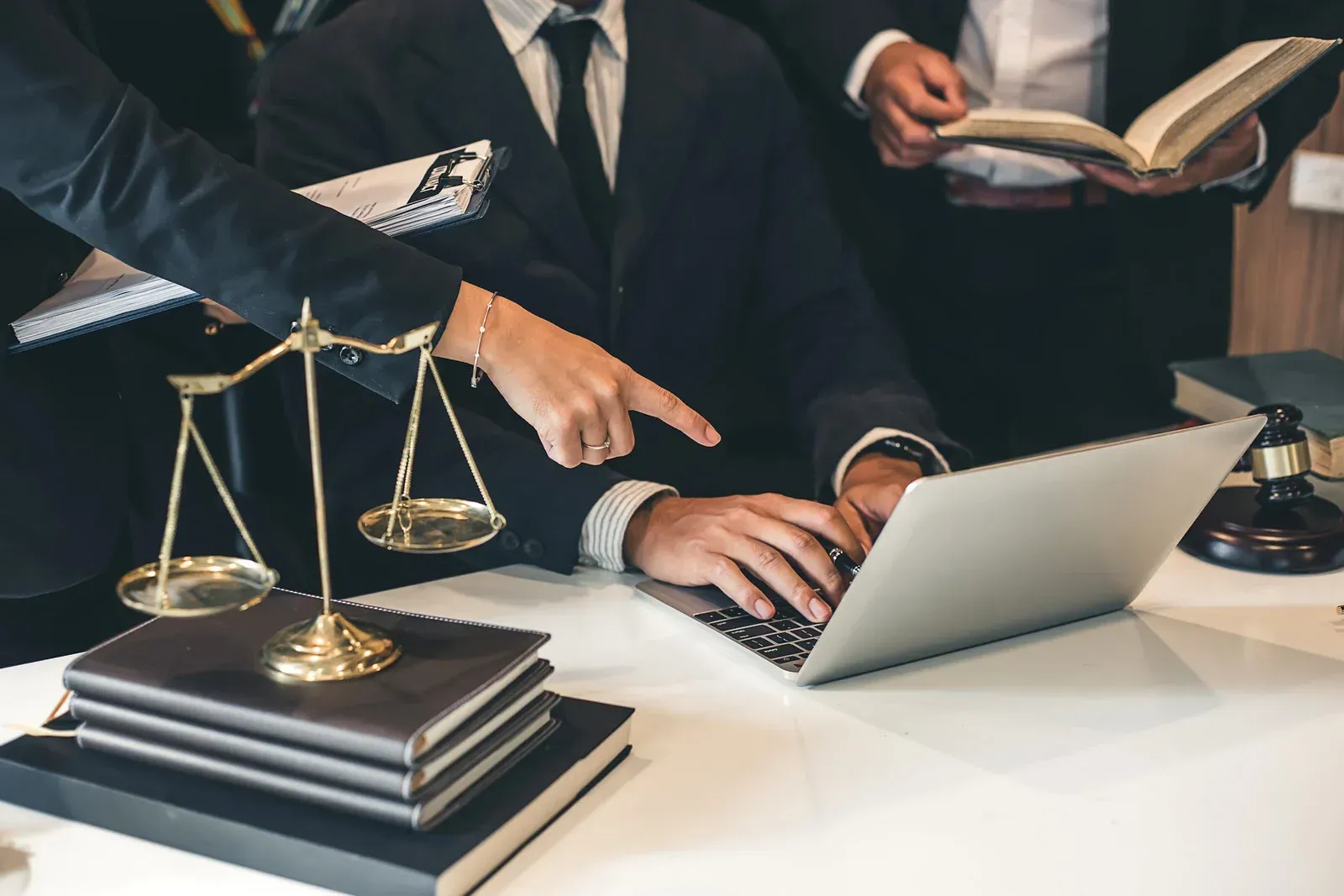 A group of lawyers are sitting at a table looking at a laptop computer.