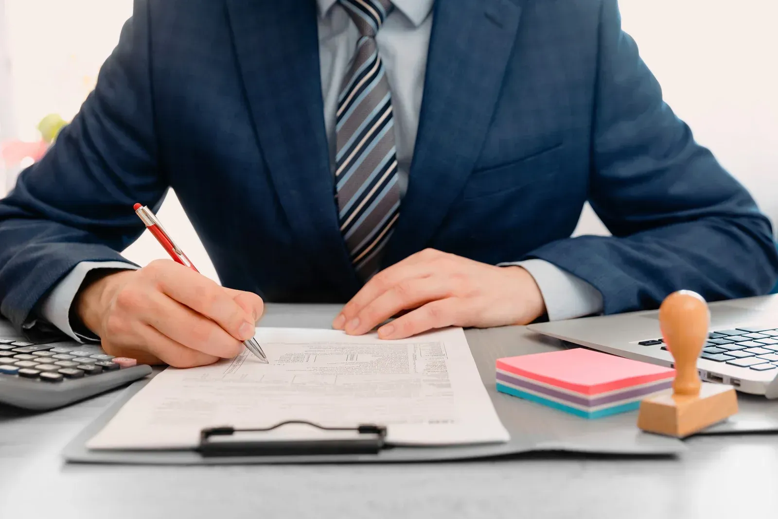 A man in a suit and tie is sitting at a desk signing a document.