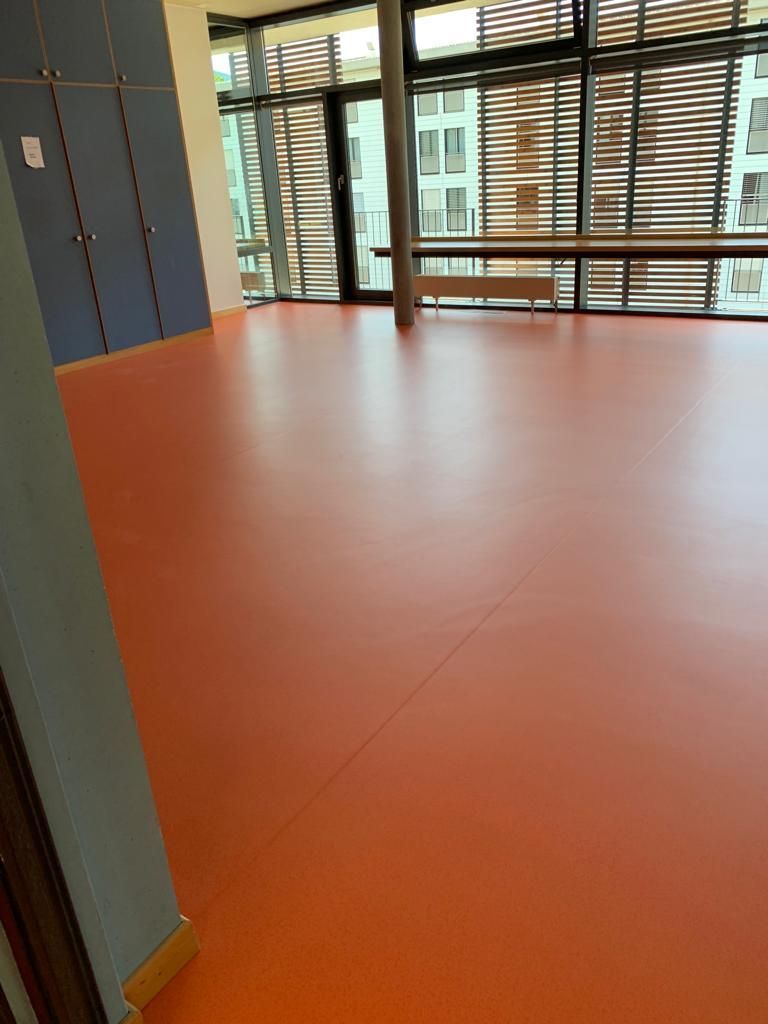 Une grande pièce avec beaucoup de fenêtres et un sol Lino/PVC rouge