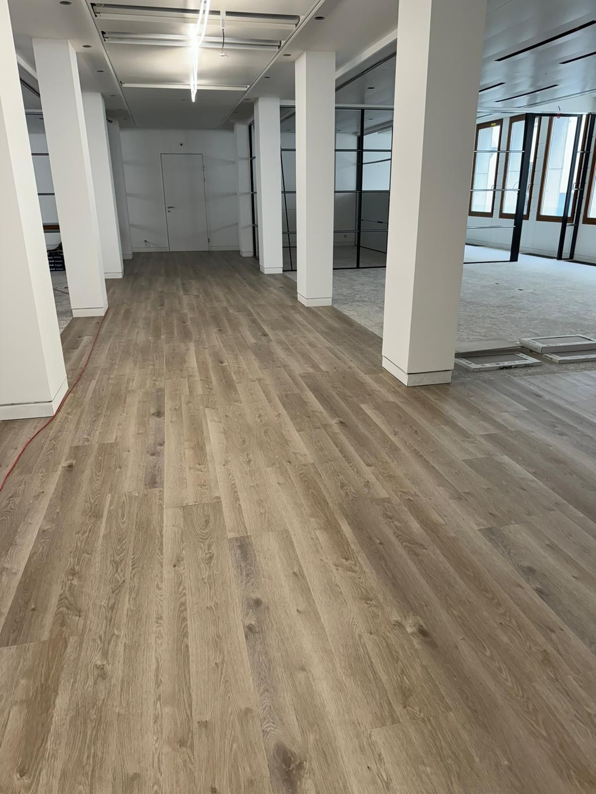 Une grande pièce vide avec un plancher en bois et des piliers blancs.