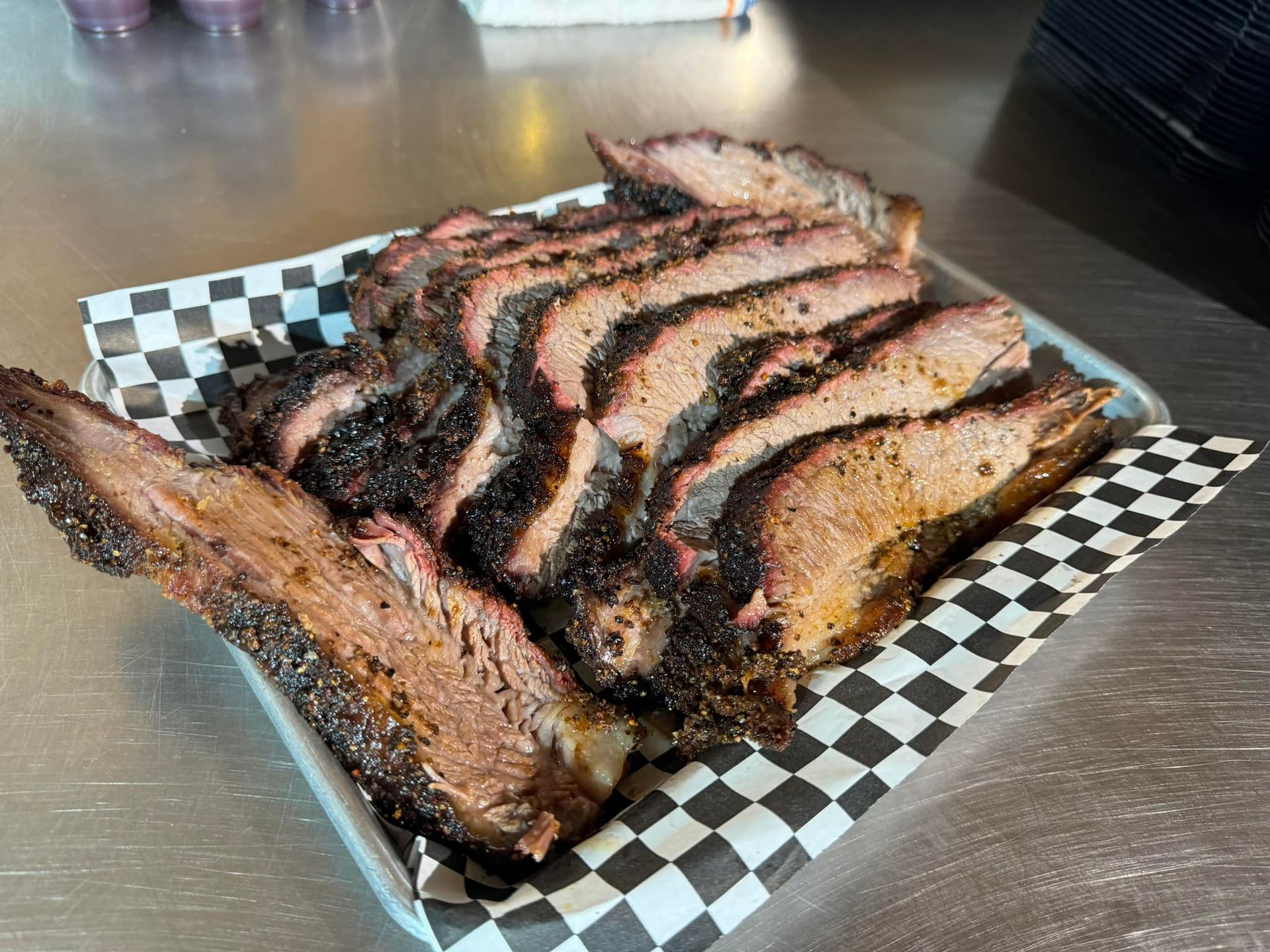 A plate of sliced meat on a checkered paper on a table.