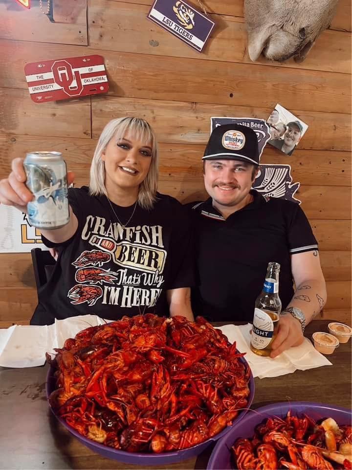 A man and a woman are sitting at a table with crawfish and beer.