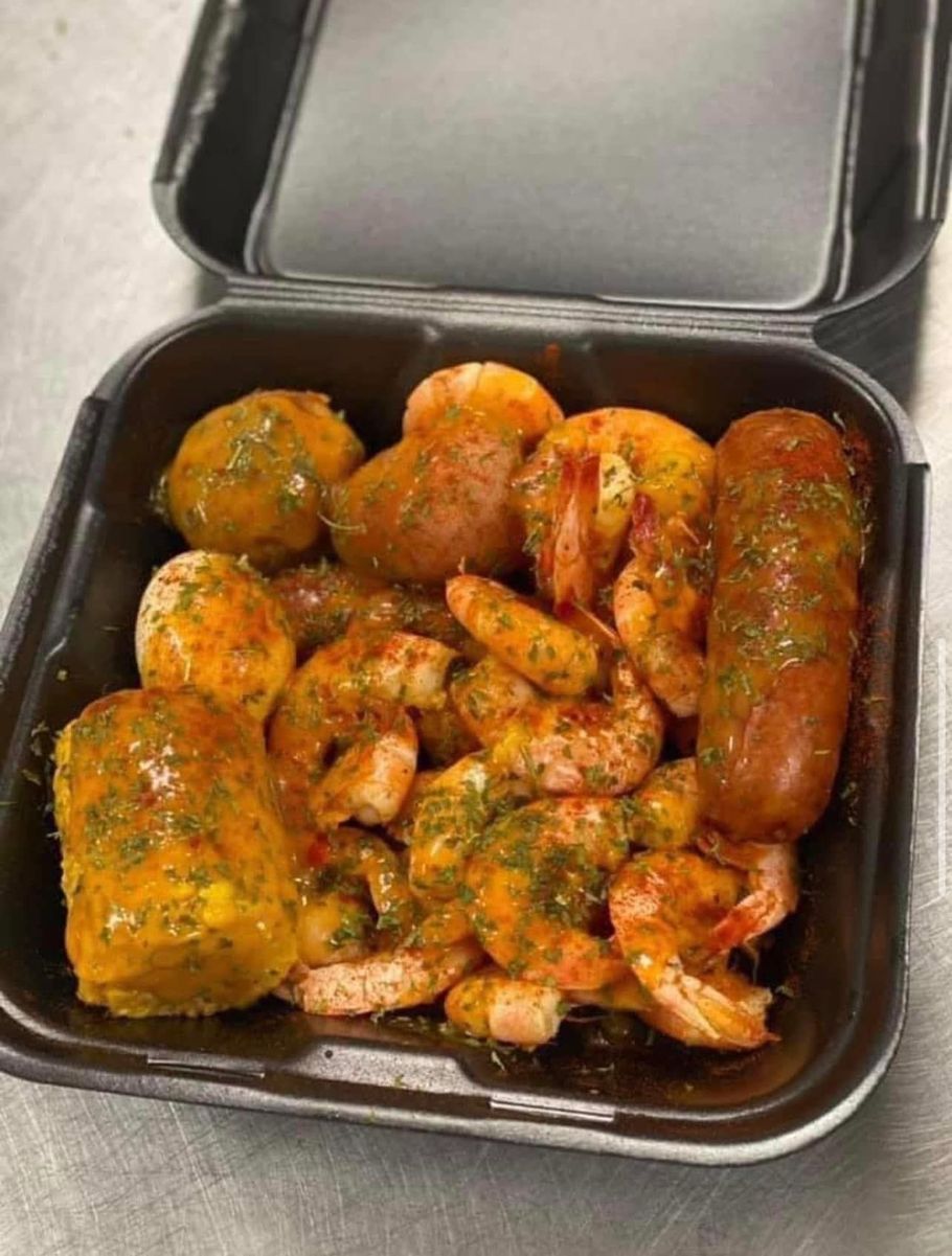 A plastic container filled with shrimp and sausage on a table.