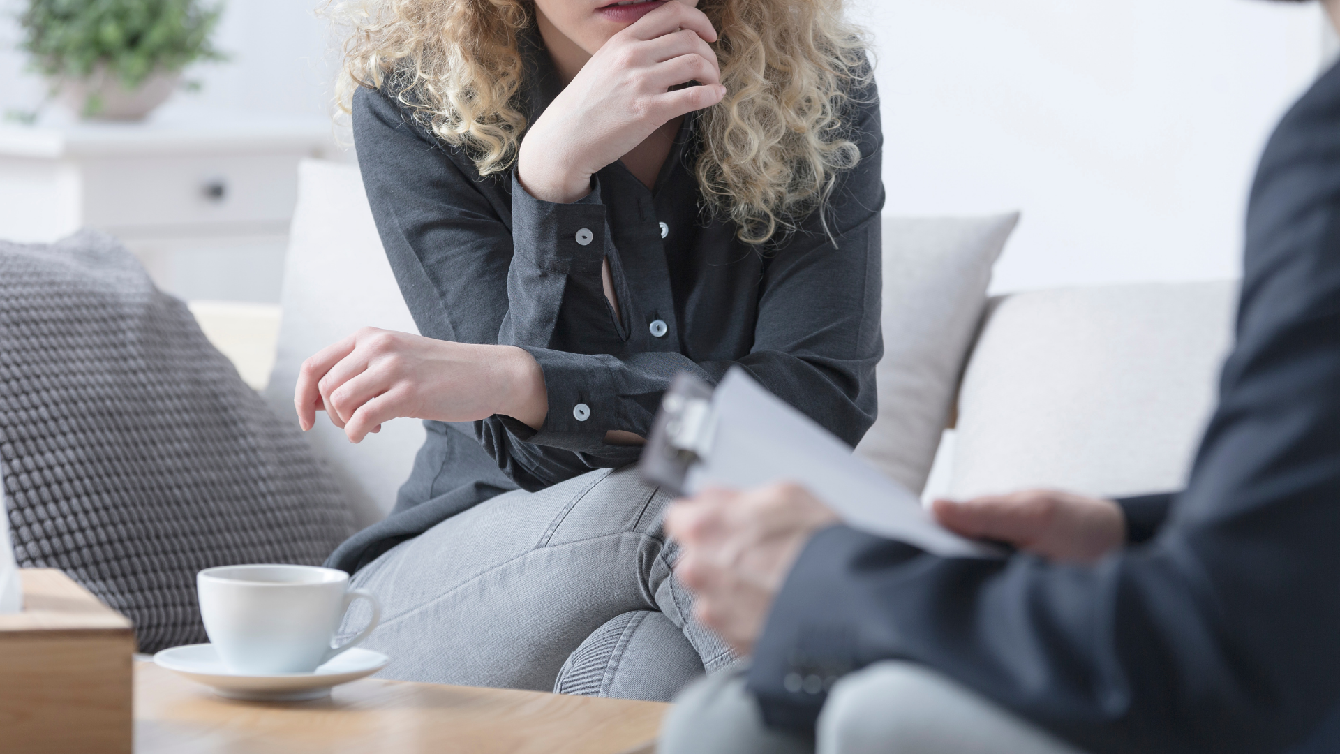 Two people talking on a sofa, with a coffee cup on the table in a bright living room