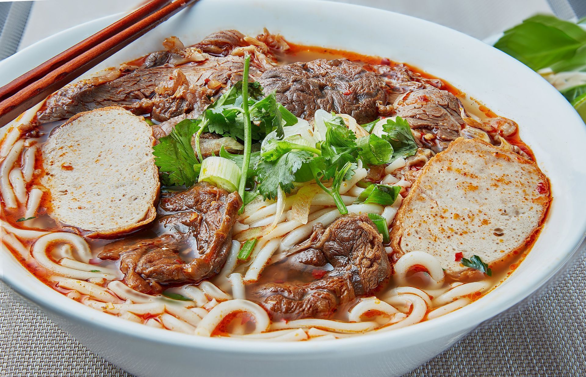 A bowl of soup with noodles , meat and chopsticks on a table.