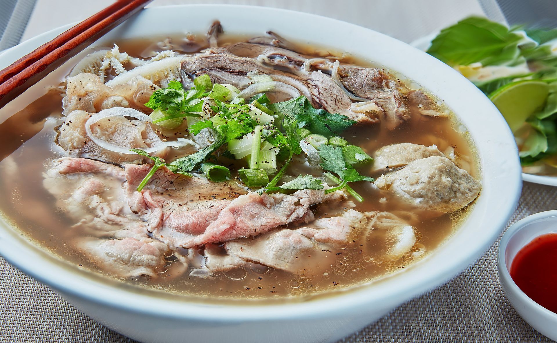 A bowl of beef noodle soup with chopsticks on a table.
