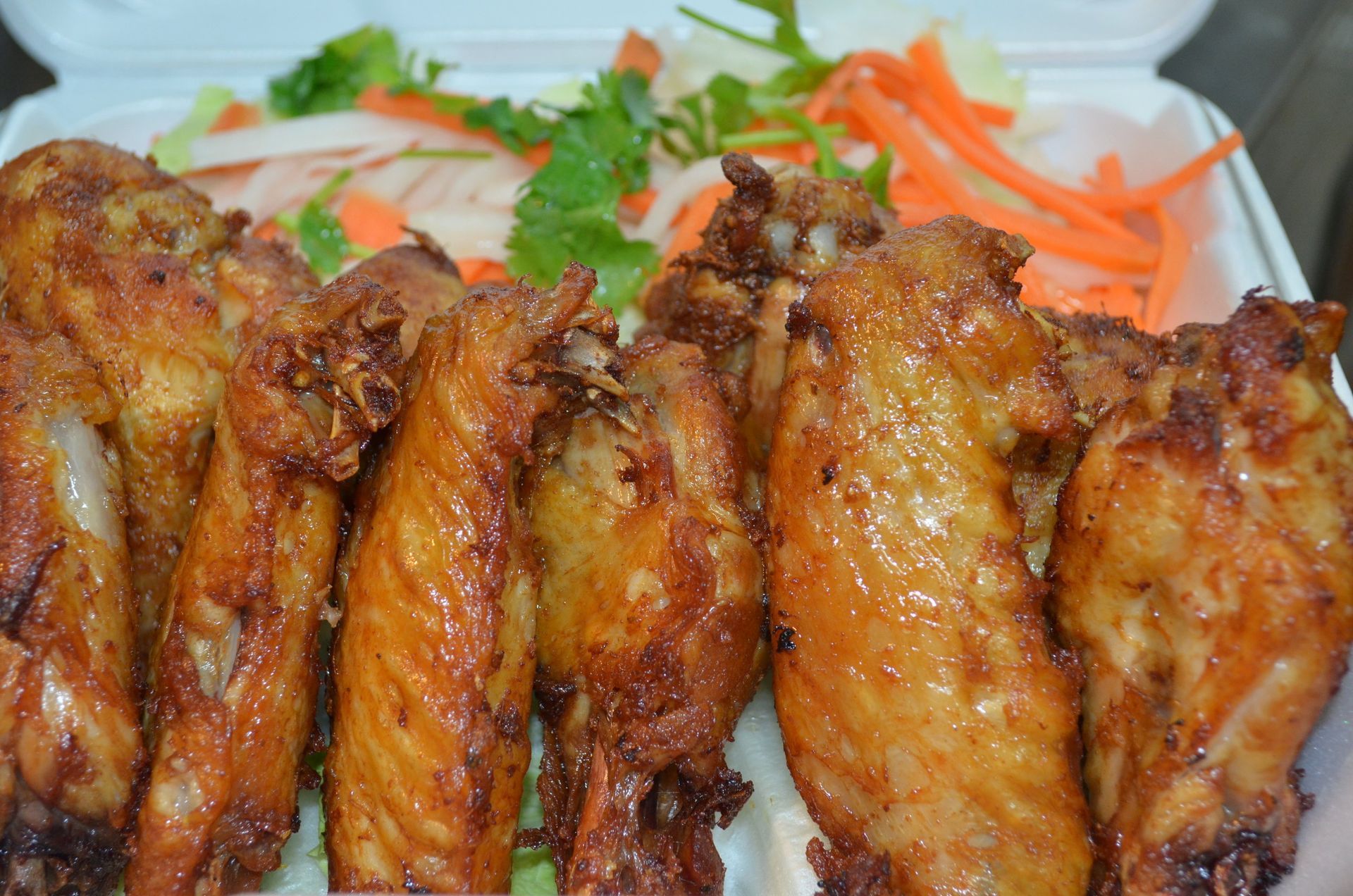 A styrofoam container filled with fried chicken wings and carrots.