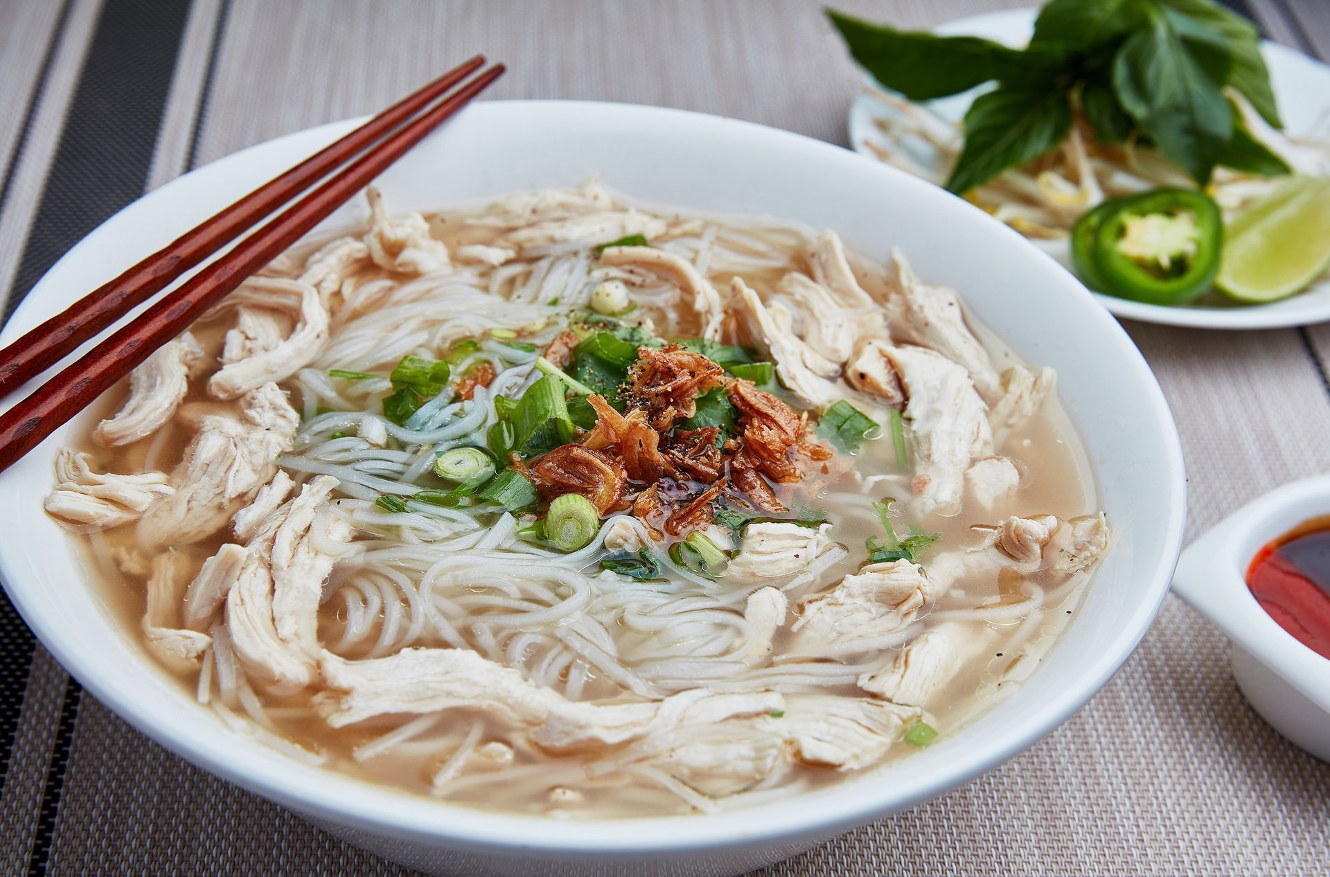 A bowl of chicken pho noodle soup with chopsticks on a table.