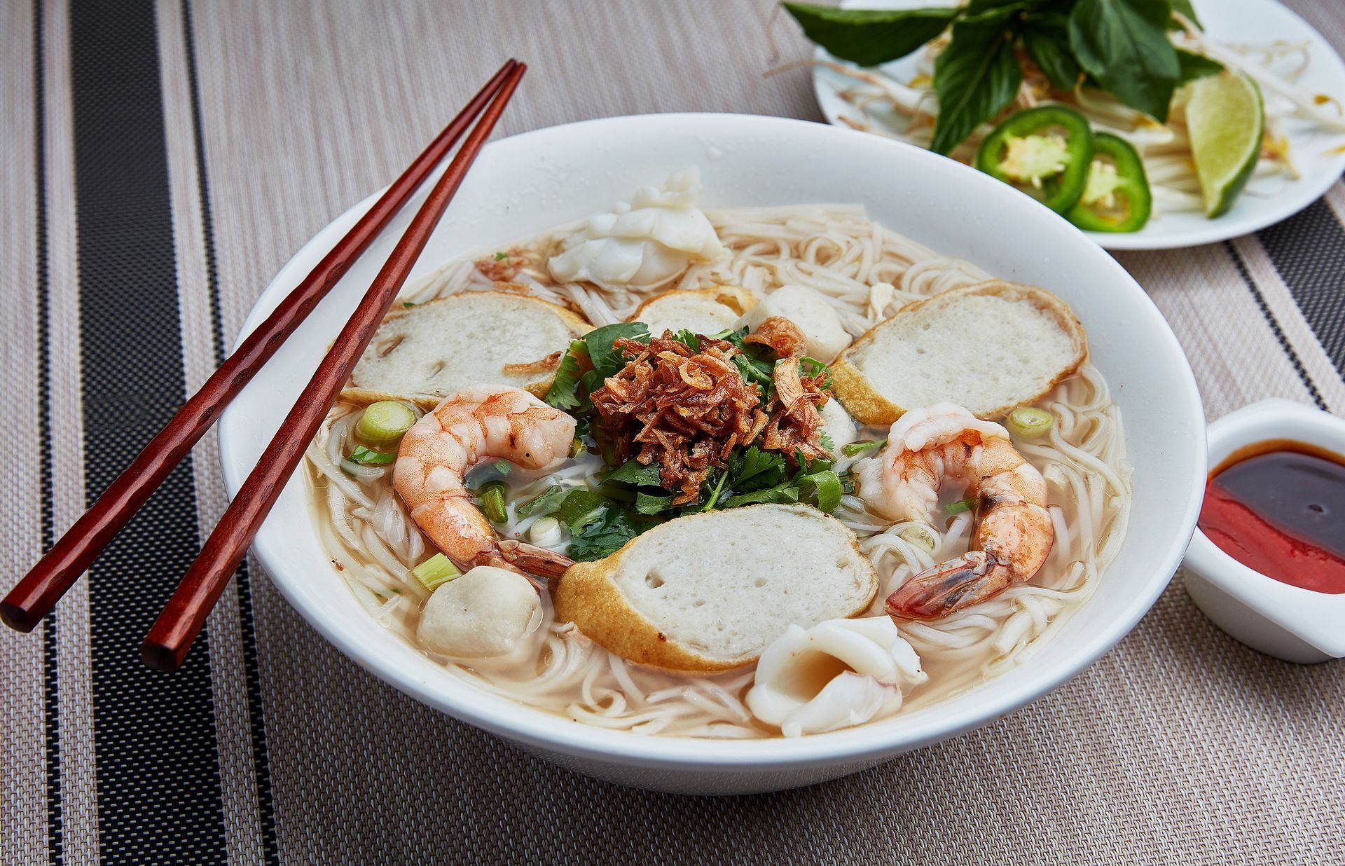 A bowl of seafood noodle soup with chopsticks on a table.