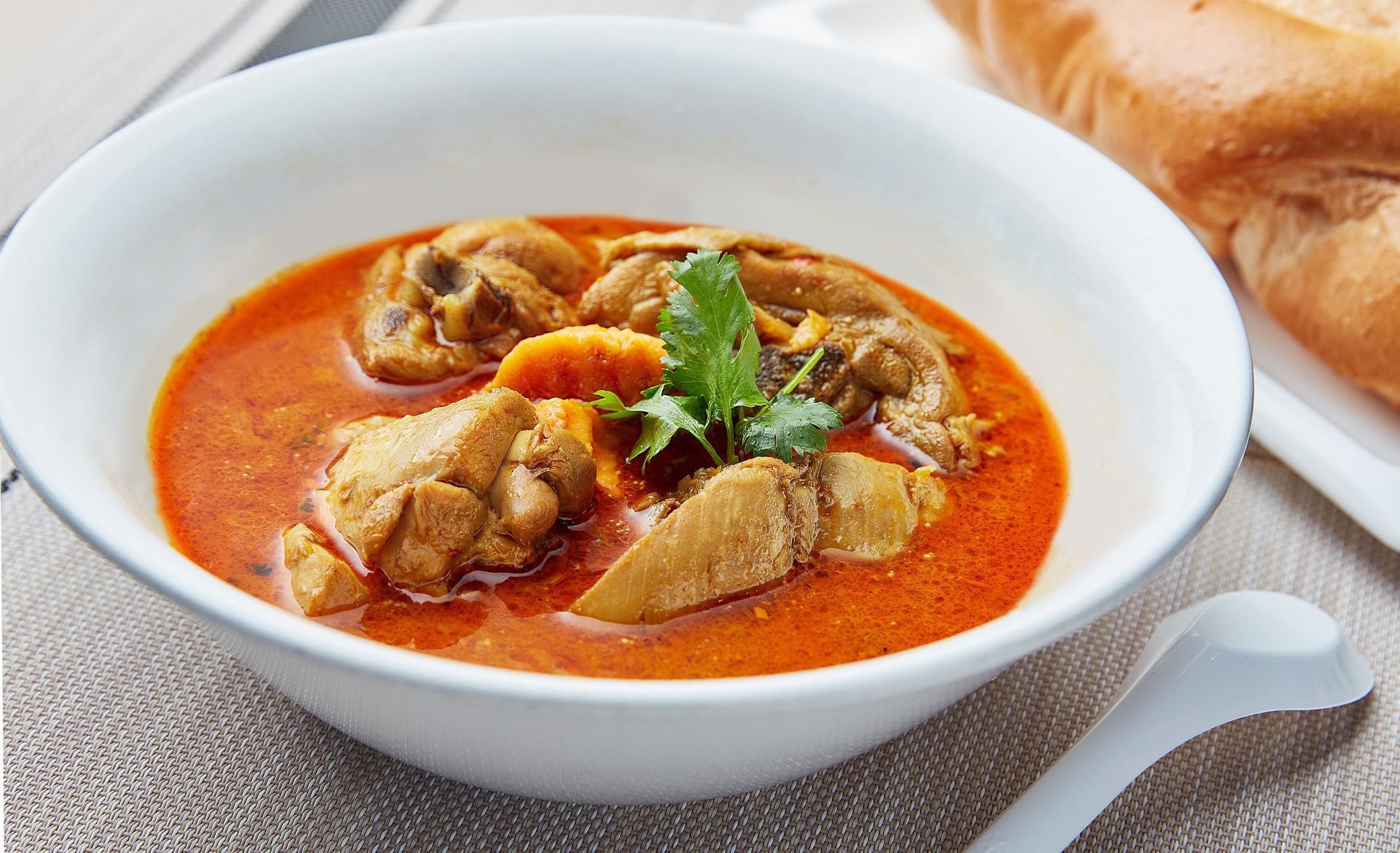 A bowl of chicken curry next to a loaf of bread