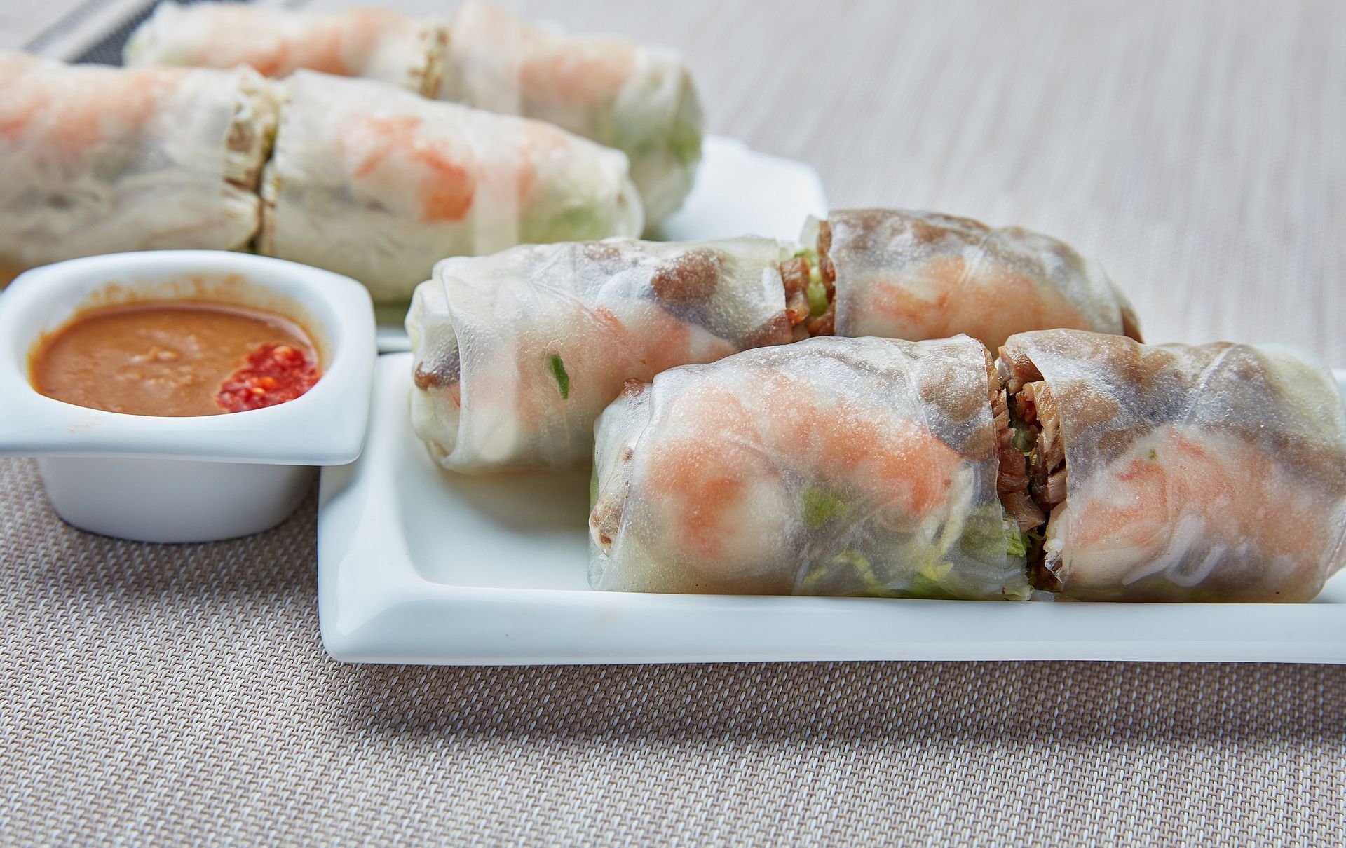 A white plate topped with rice rolls next to a bowl of dipping sauce.
