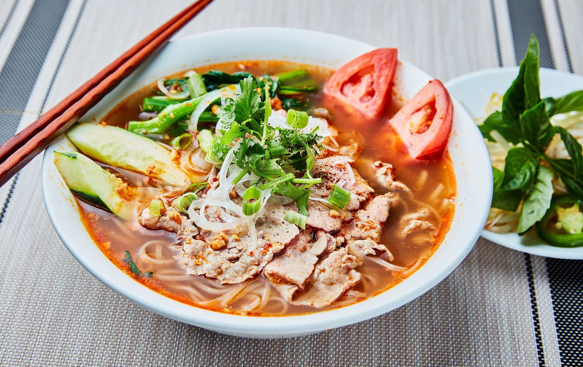 A bowl of soup with meat and vegetables on a table with chopsticks.