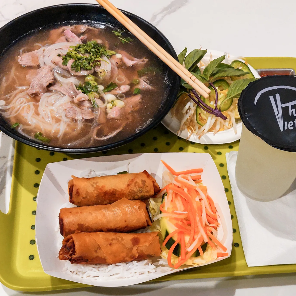 A tray of food including a bowl of Phở and spring rolls