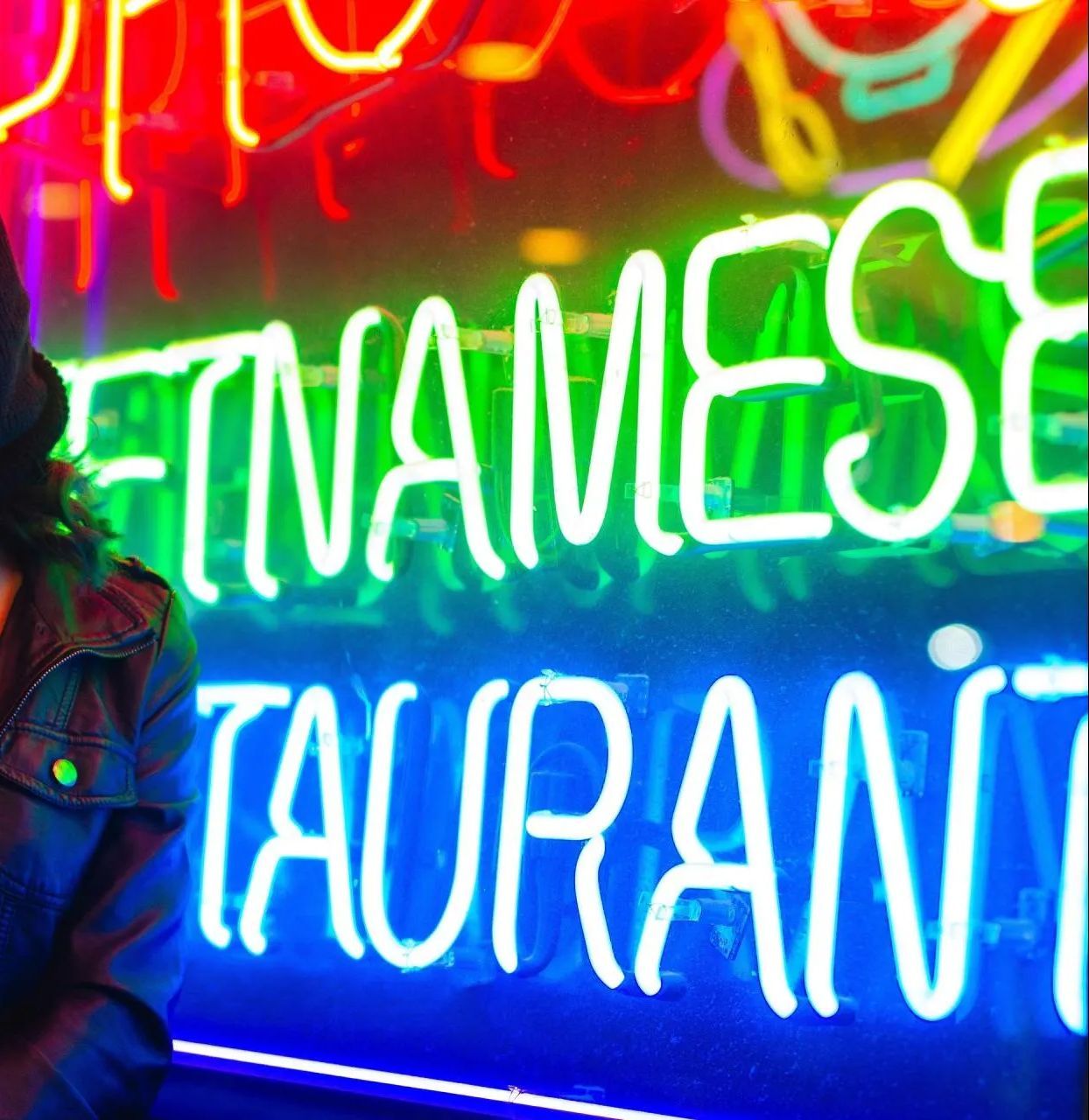A woman wearing a ski mask is standing in front of a neon sign that says vietnamese restaurant