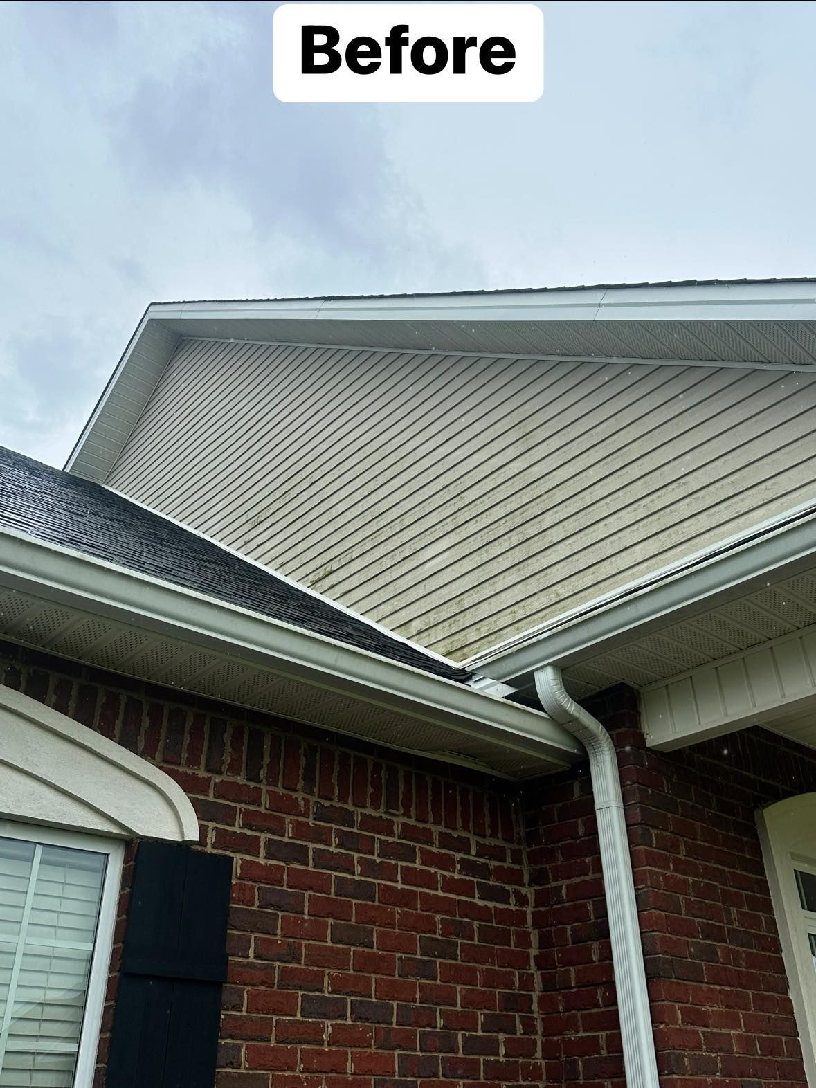 A before picture of a brick house with white siding and black shutters.