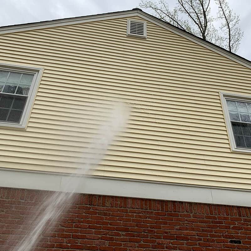 A person is using a high pressure washer to clean the side of a house.